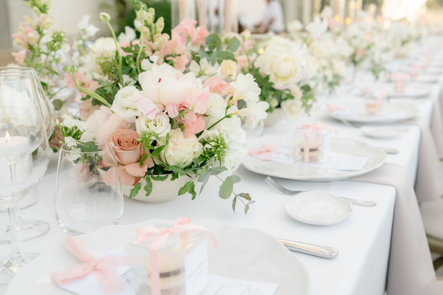 Elegant wedding reception table settings with blush pink and white floral centerpieces and crystal glassware.