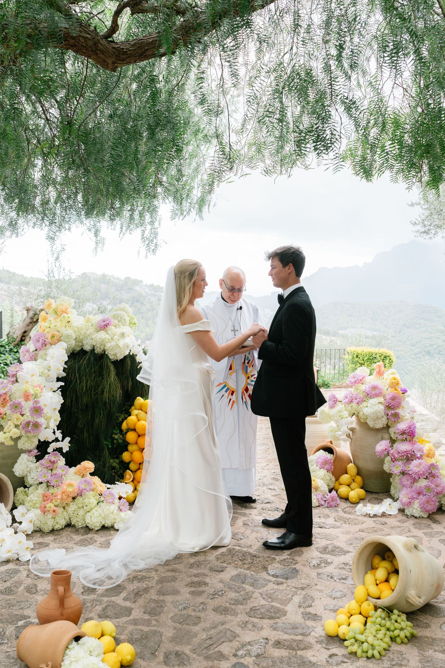 Outdoor wedding ceremony setup with floral arrangements and yellow accents under a willow tree.