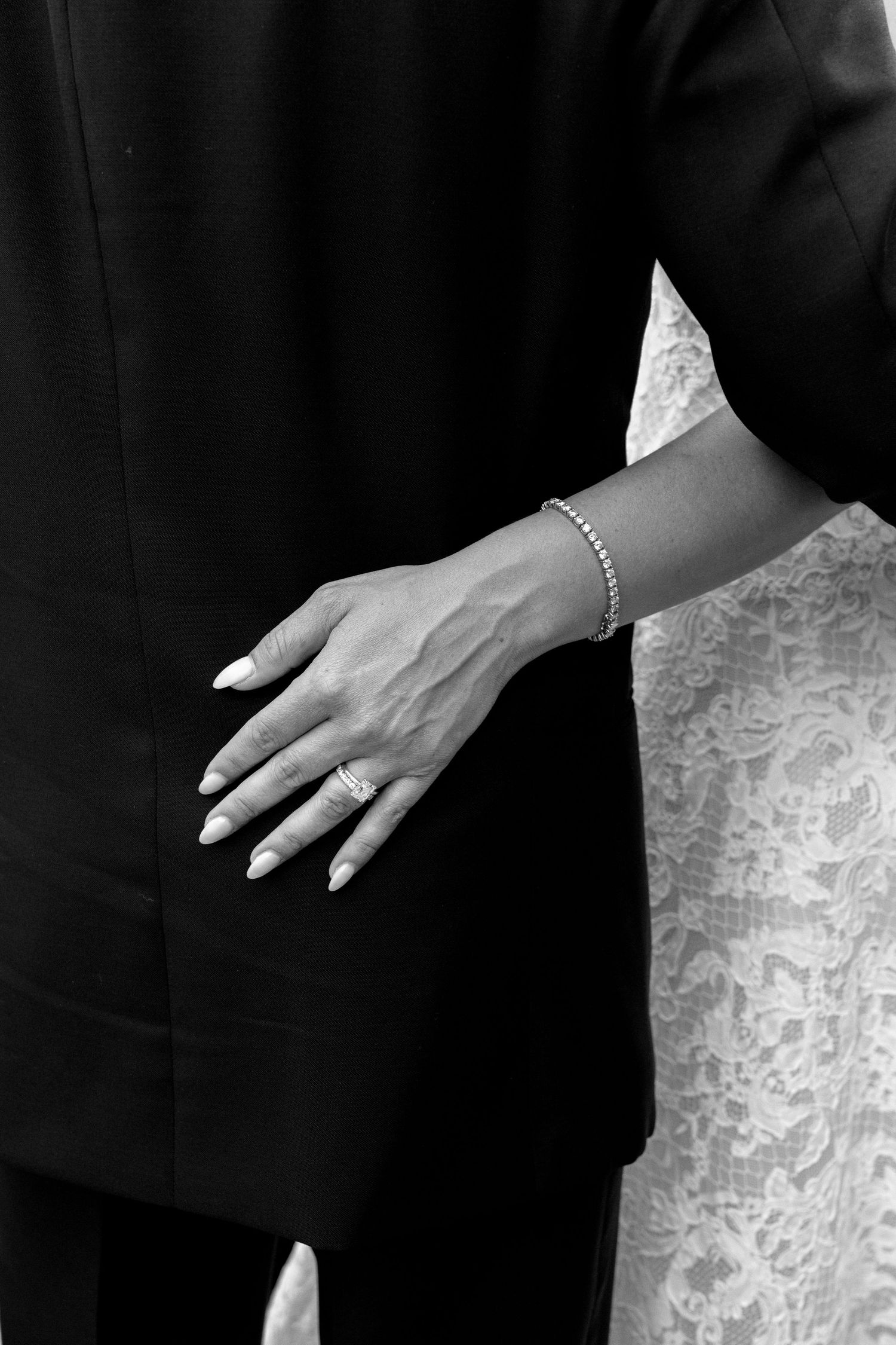 Black and white photo of a bride's hand with wedding ring and bracelet resting on groom's suit jacket.
