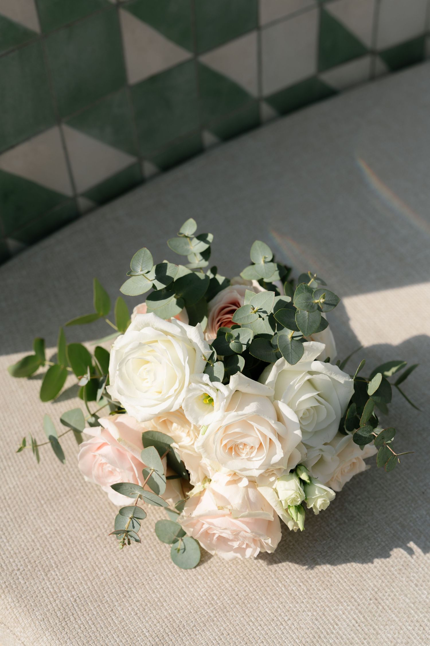 Delicate white roses and eucalyptus arrangement on textured grey surface.