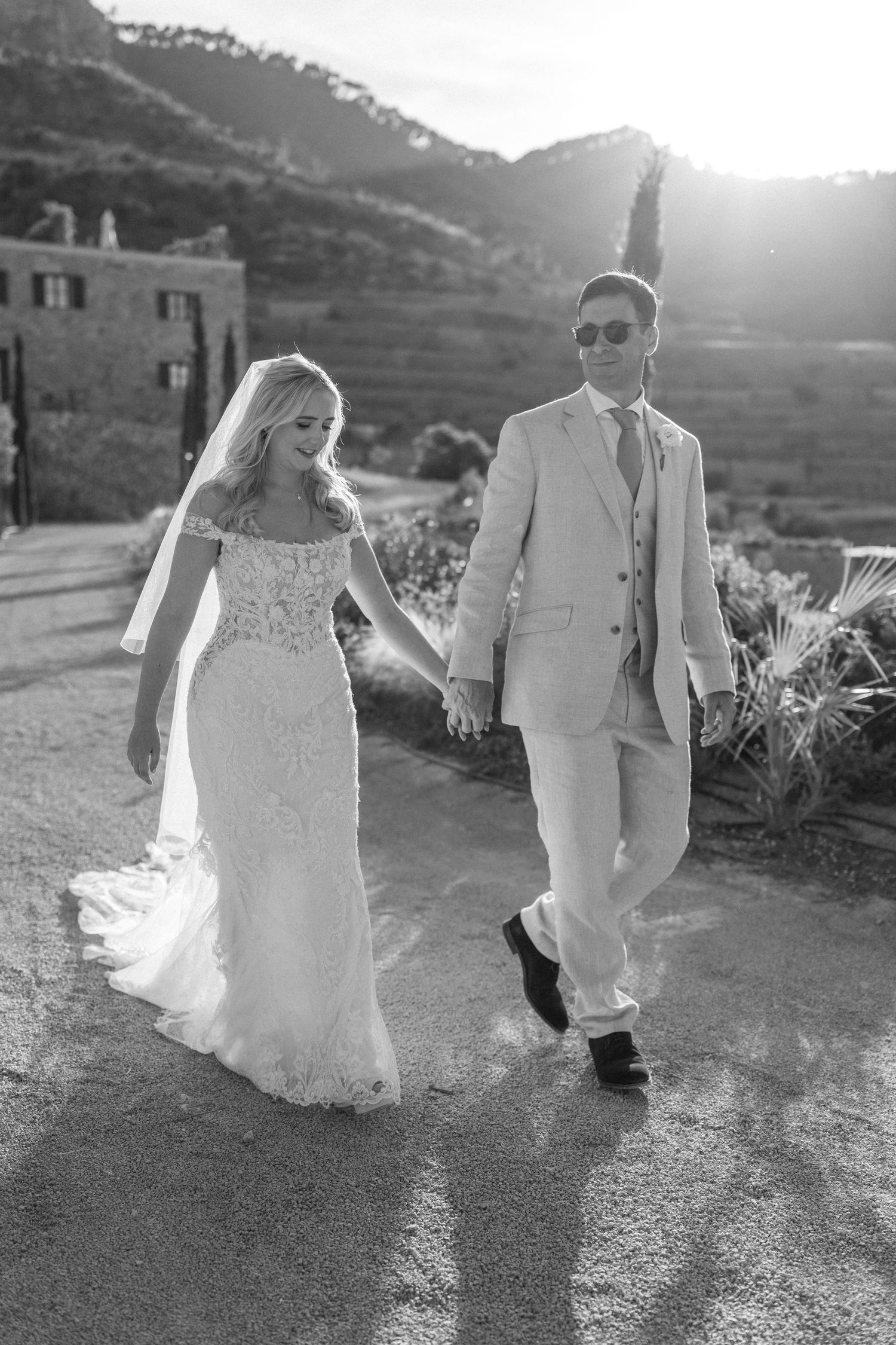 Sunset silhouette of wedding couple walking along mountain path in black and white.