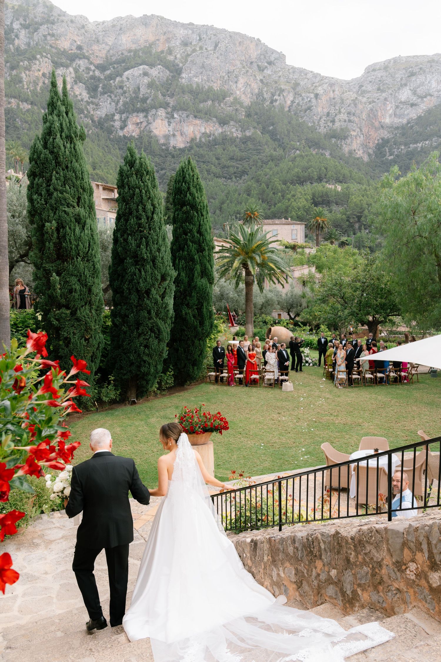 Scenic mountain wedding ceremony setup with cypress trees and red floral accents.