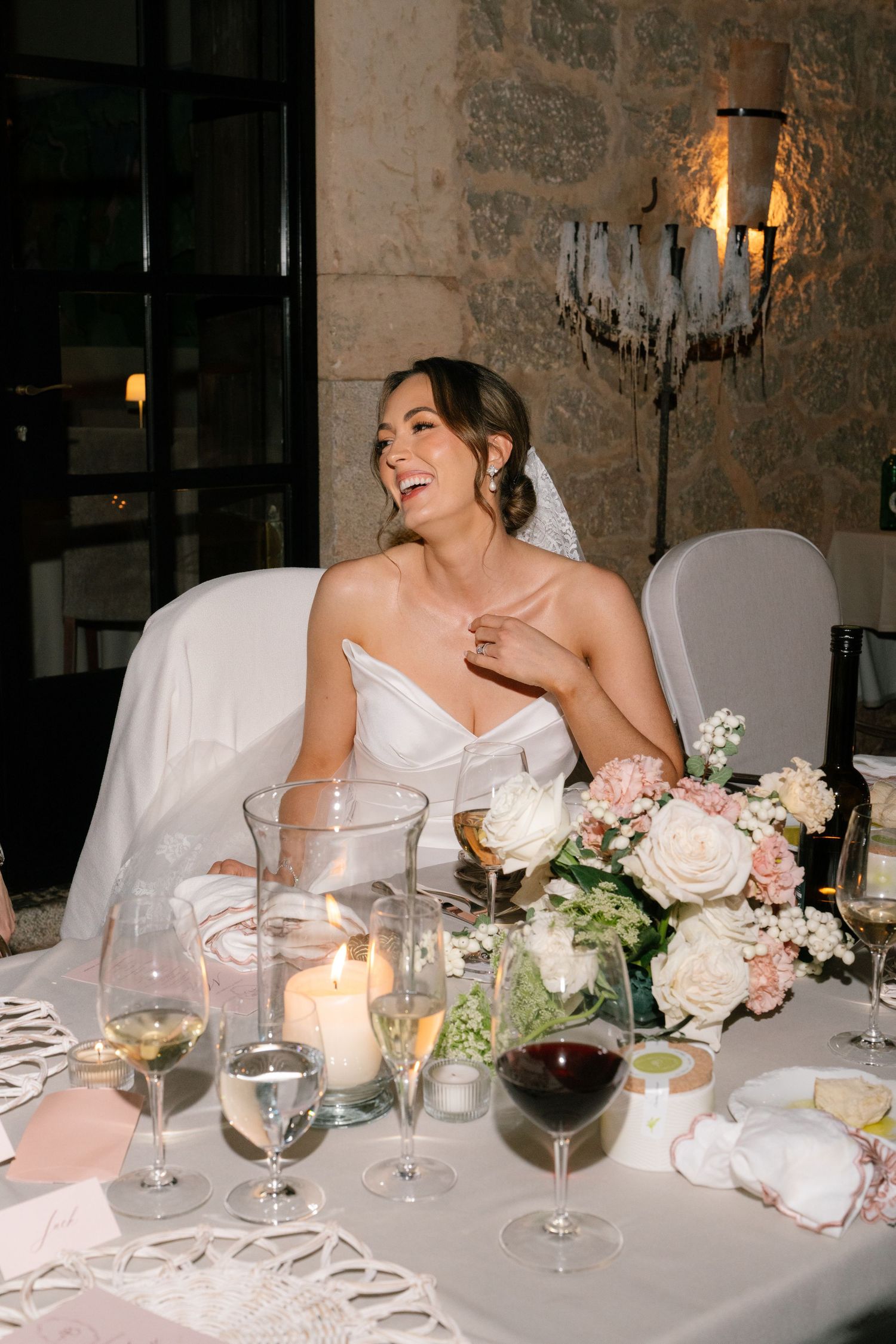 Elegant wedding reception table setting with champagne glasses, candles and blush floral centerpiece at stone-walled venue.