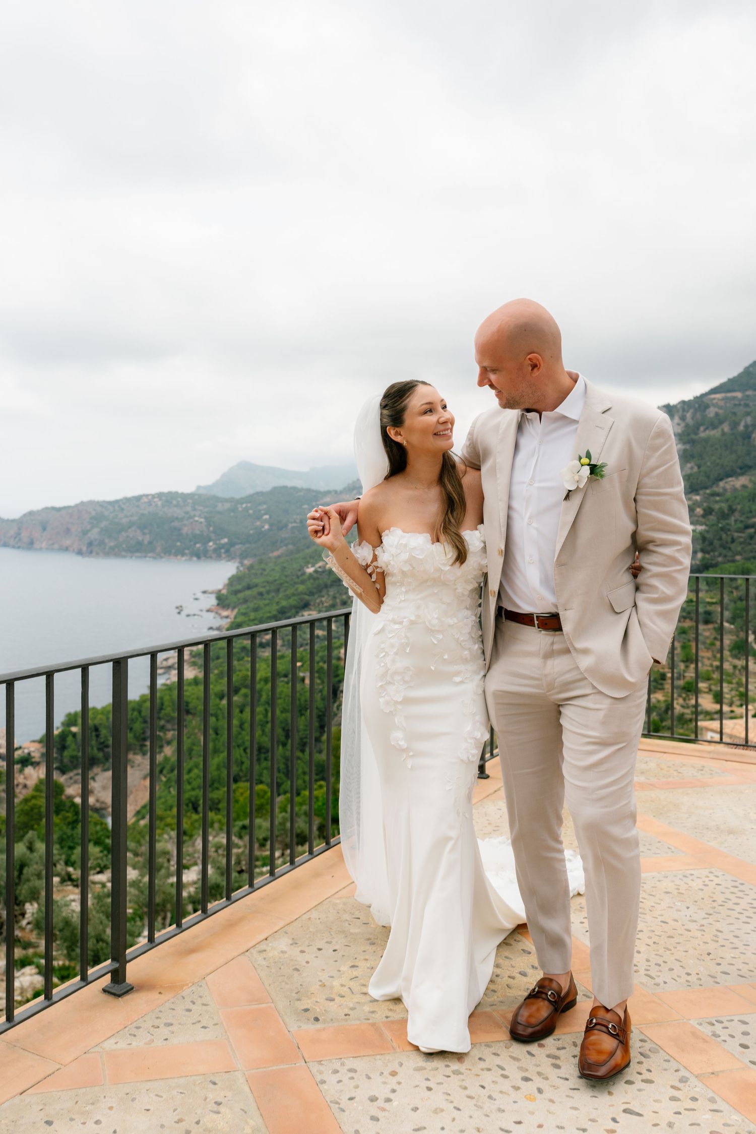 A romantic wedding couple shares a moment on a terrace overlooking scenic coastal mountains.