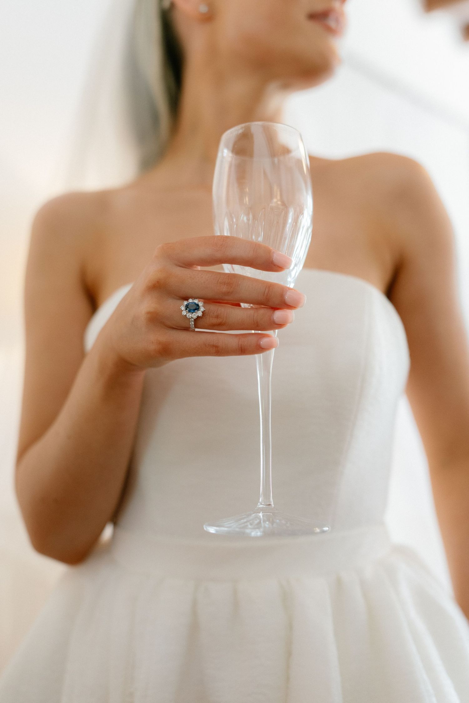 Elegant close-up of champagne glass held by someone in a white wedding dress.