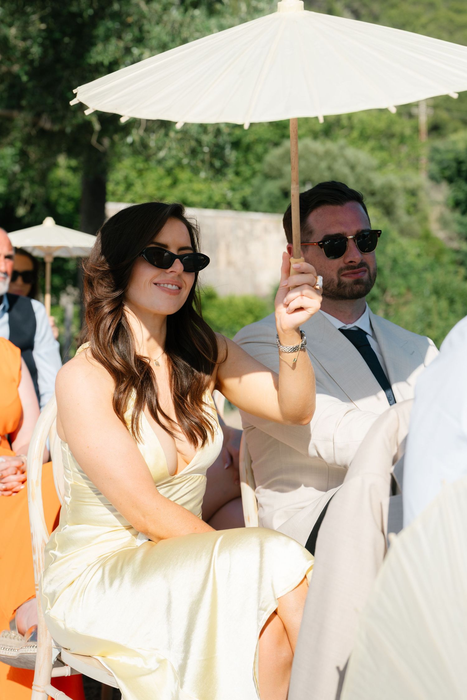 Wedding party with parasols in light summer attire at outdoor venue.