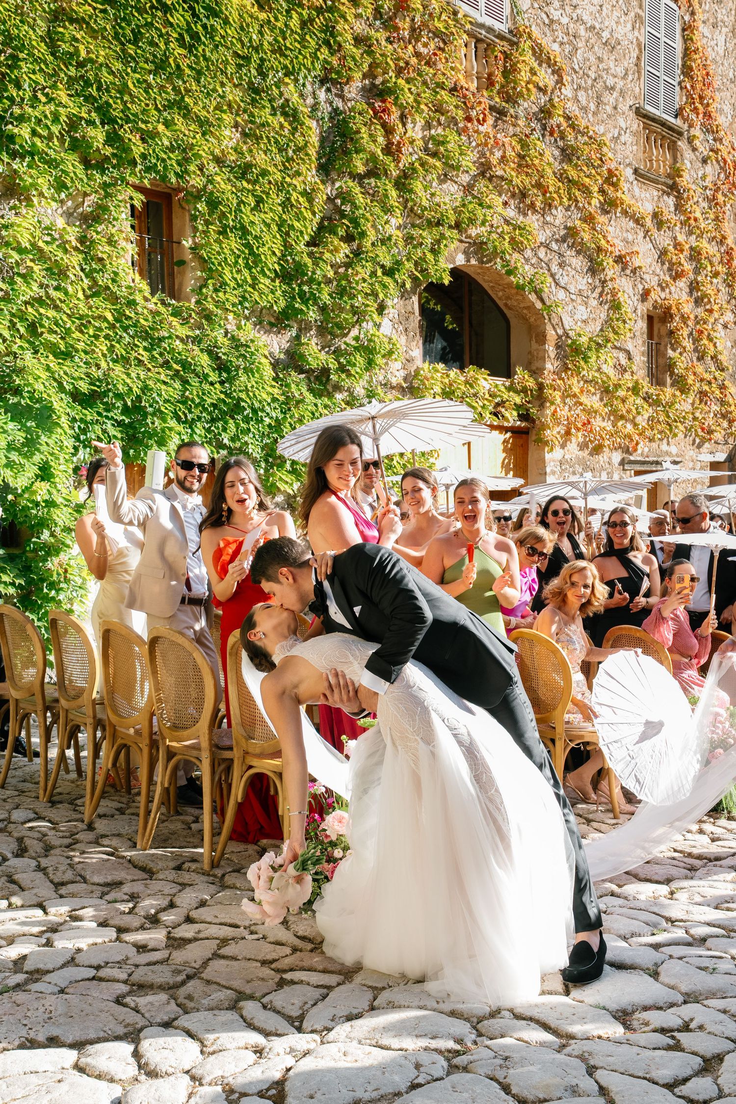 Wedding celebration on rustic stone patio with ivy-covered walls and white chairs.