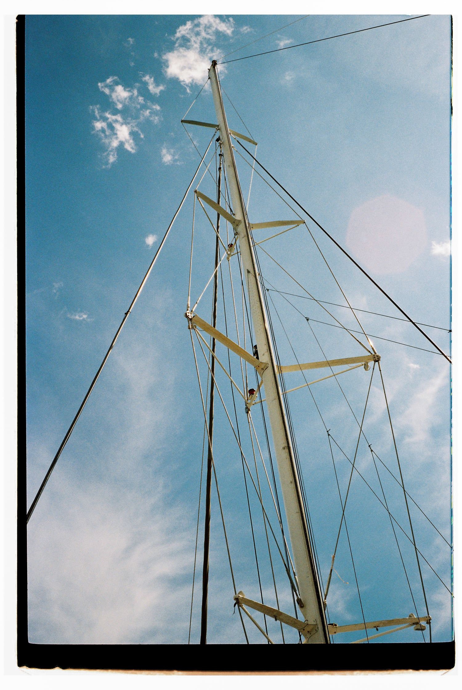 Sailboat masts and rigging against a bright blue sky with white clouds.