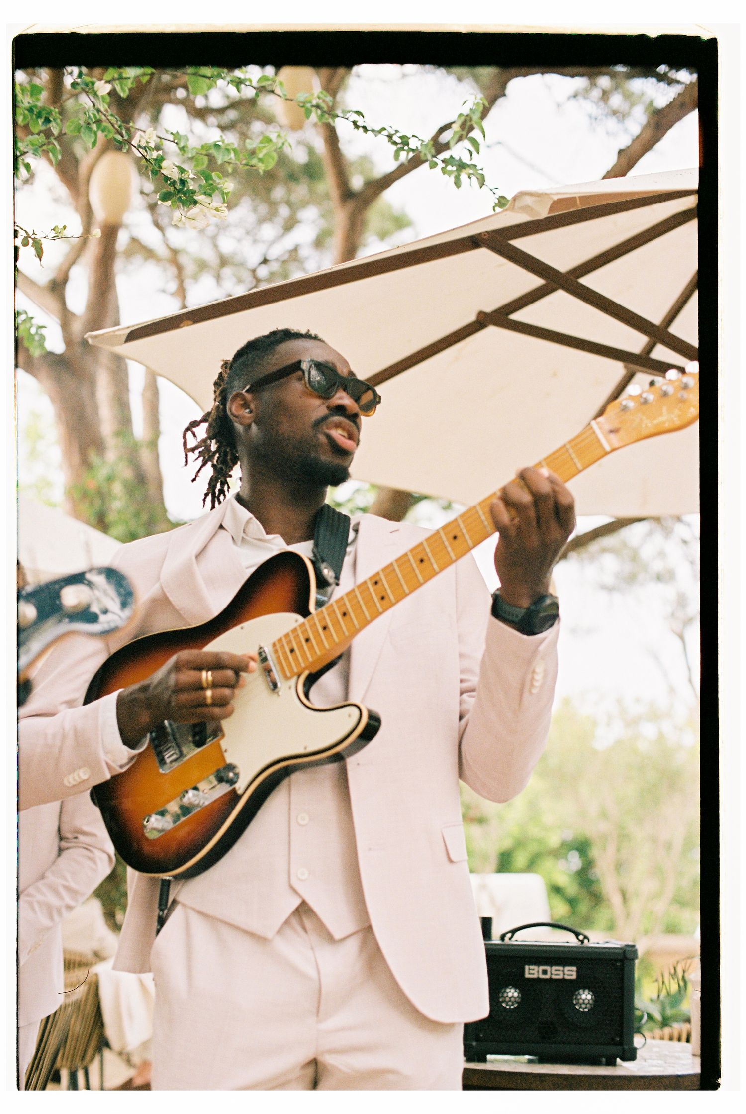 Musician in white suit playing electric guitar during outdoor performance.