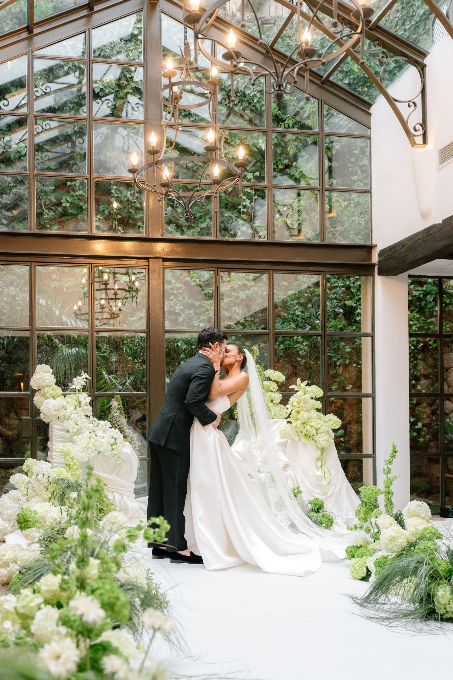 A romantic greenhouse wedding ceremony setup with white floral arrangements and hanging lights.