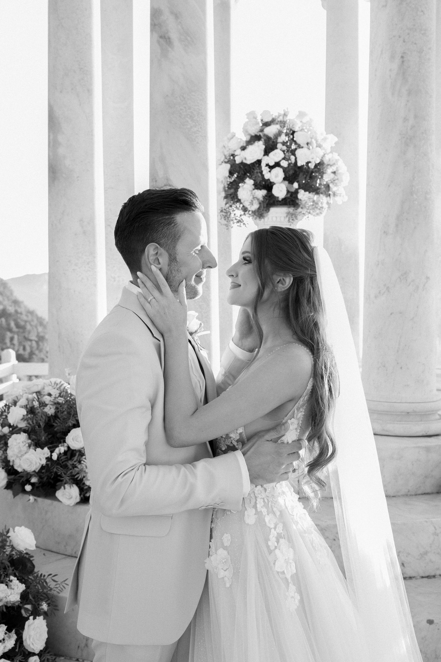 Romantic black and white portrait of newlyweds embracing between classical white columns.