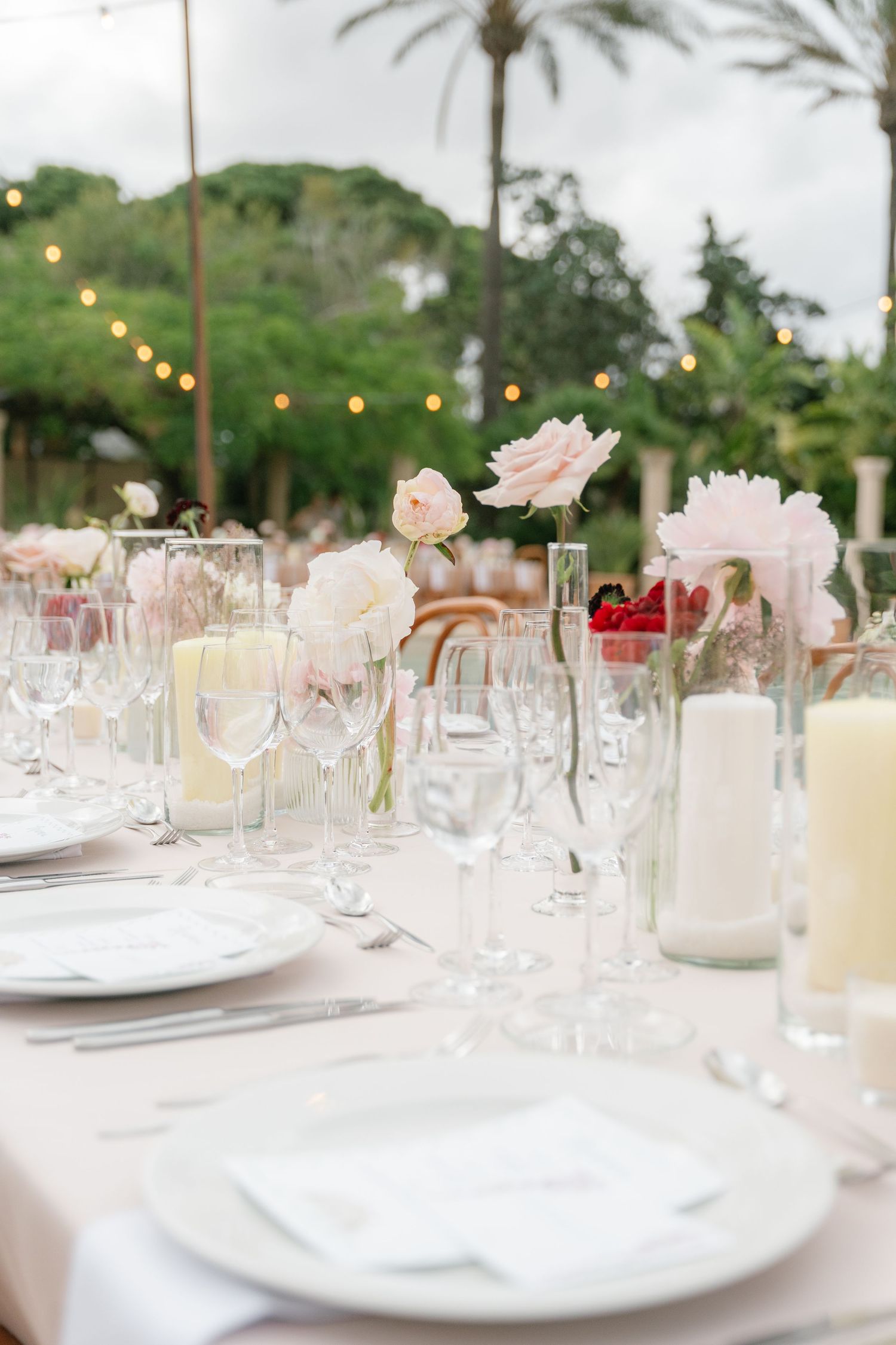 Elegant table settings with wine glasses, white linens, and delicate pink floral centerpieces.