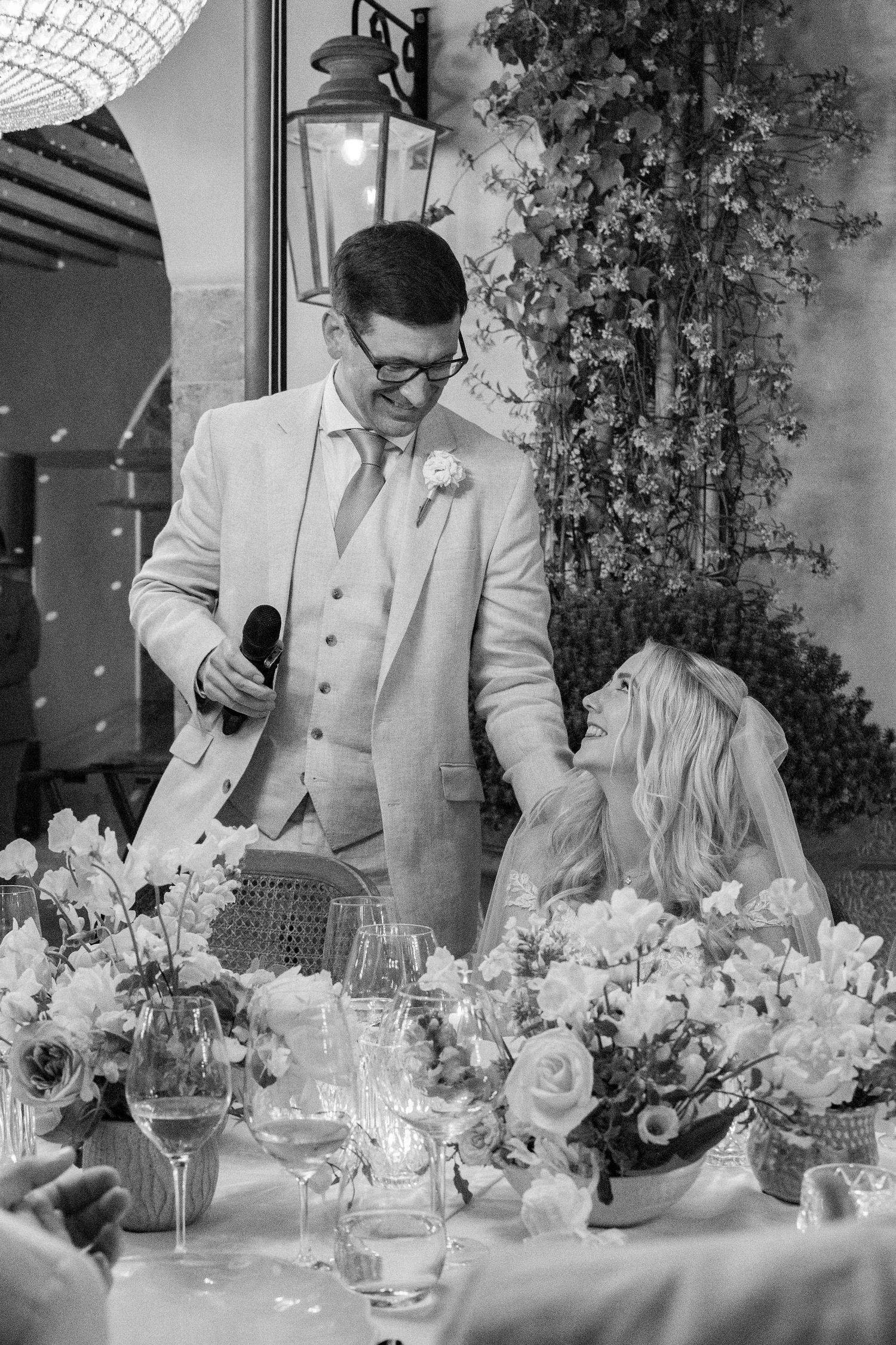 Wedding reception table with guests in light colored attire and floral decorations.