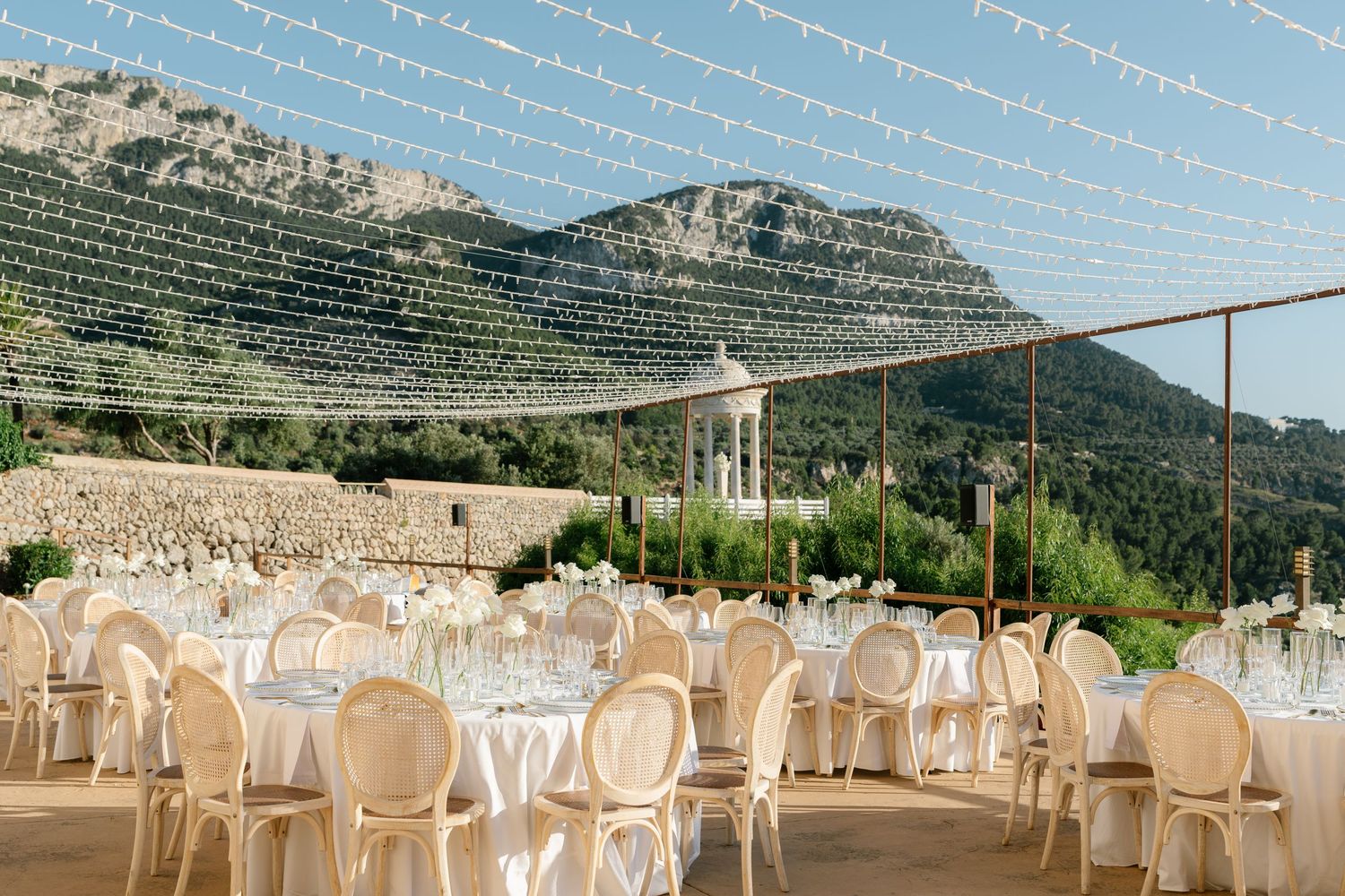Outdoor wedding venue with string lights and white chairs against a mountainous backdrop.