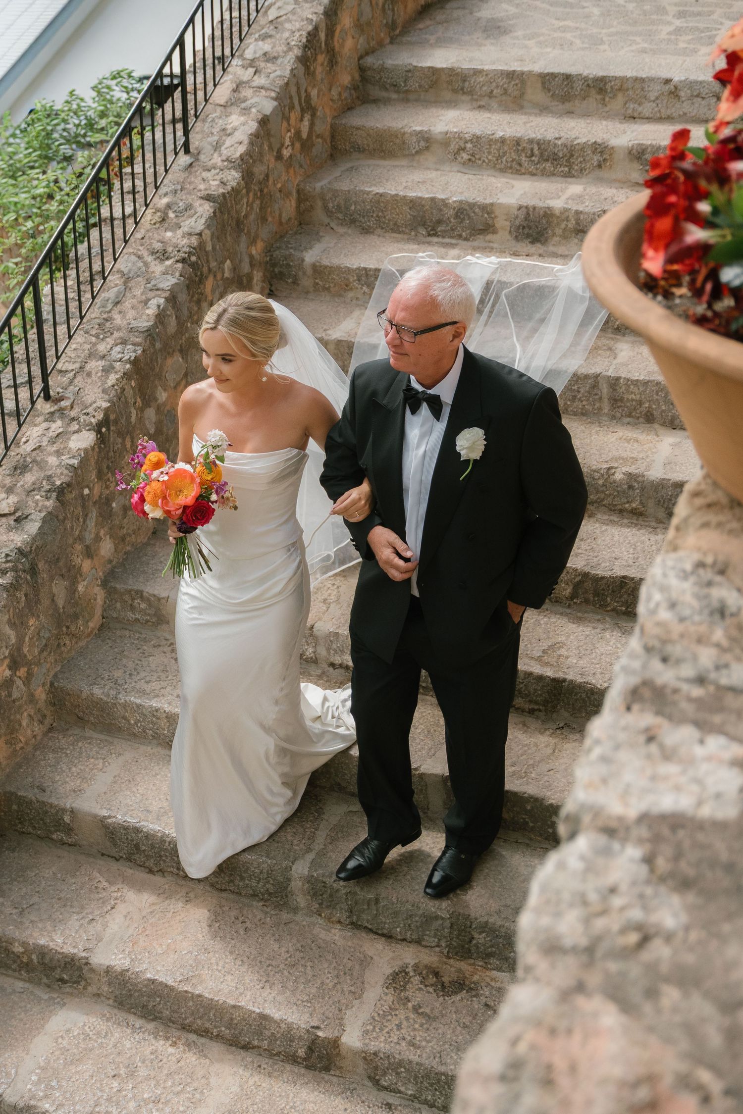 Wedding processional on stone steps decorated with red floral arrangements.