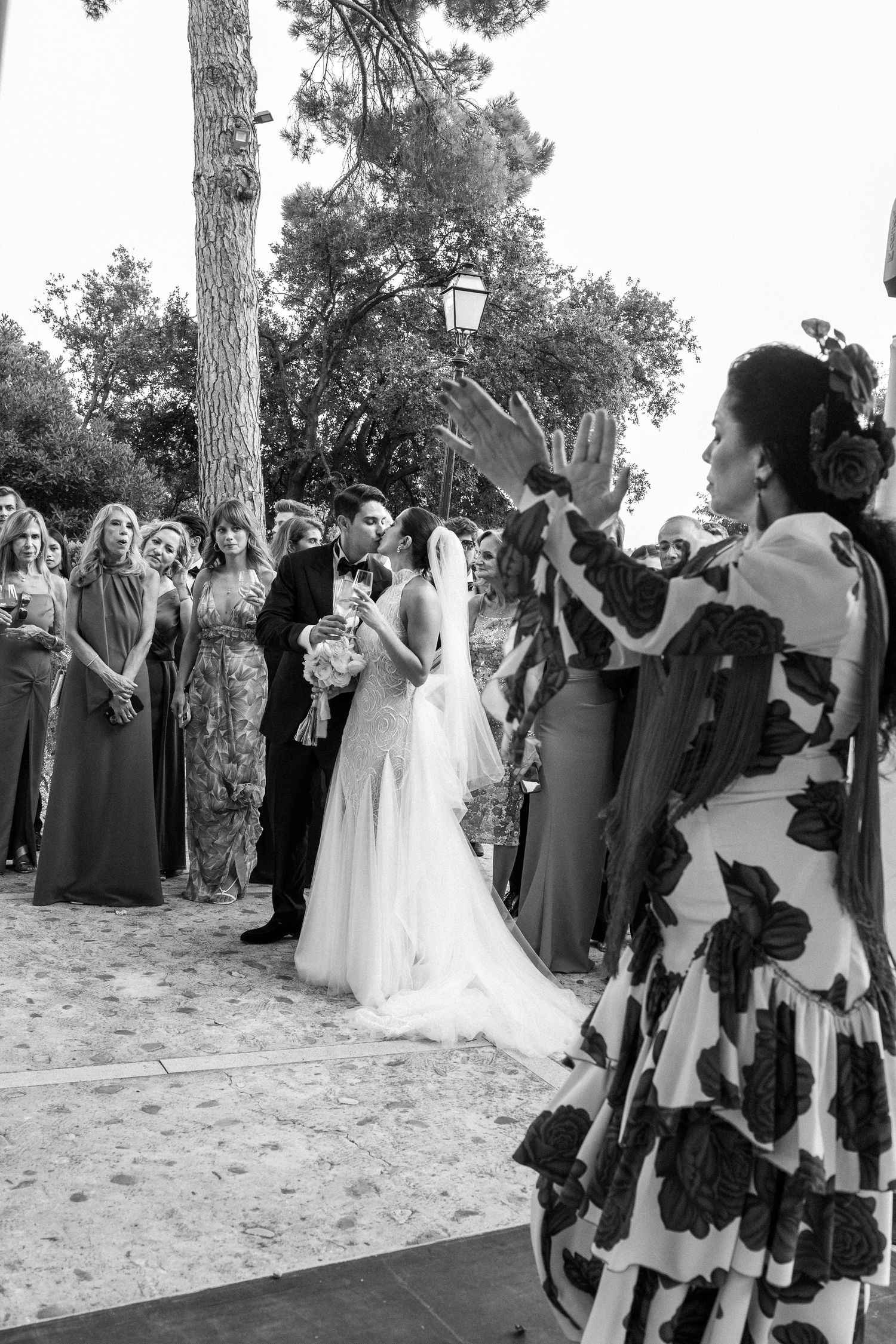 Wedding party and guests lined up outdoors under trees for a celebratory moment.