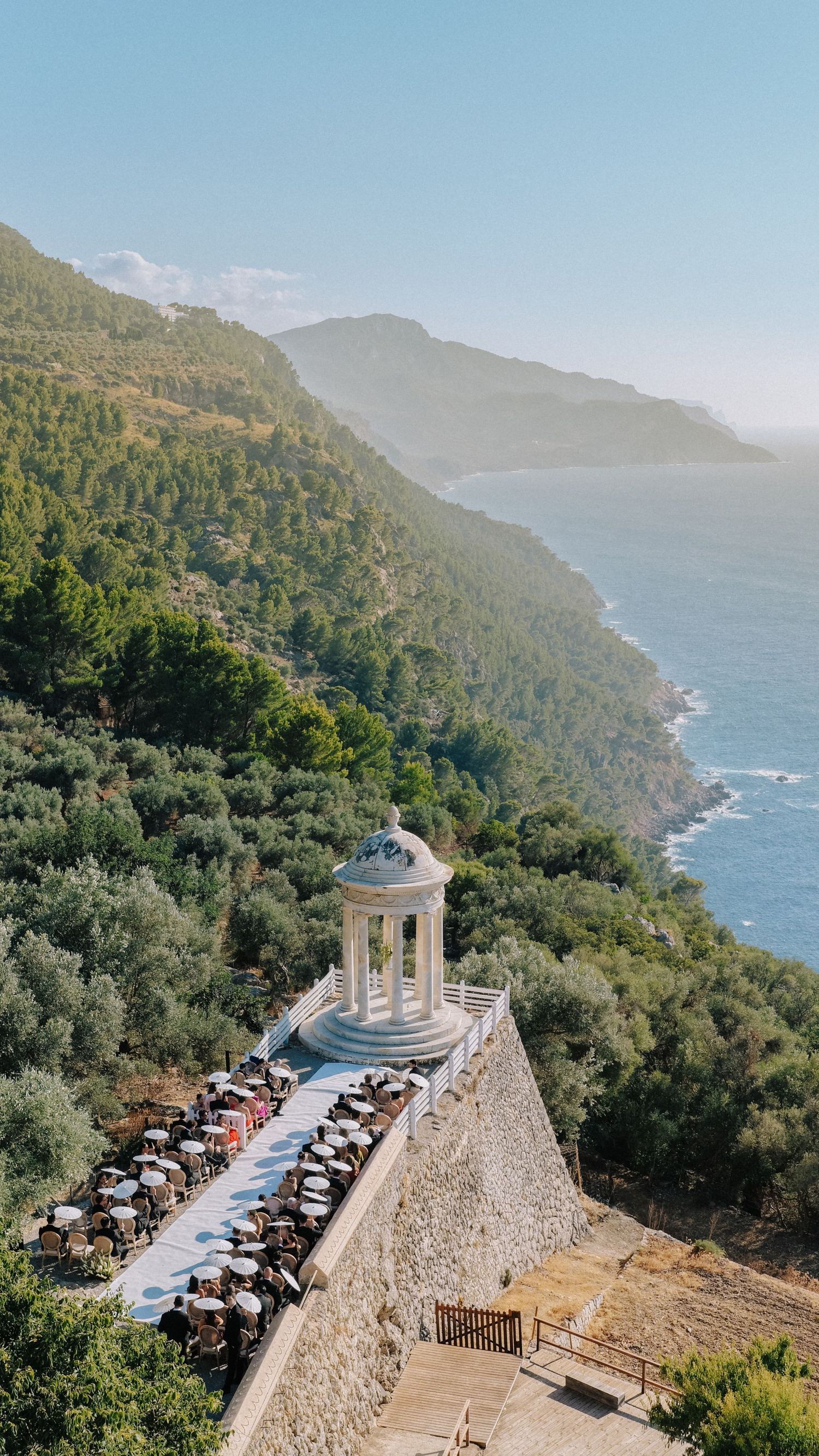 Scenic coastal terrace with white gazebo overlooking lush green mountains and blue Mediterranean sea.