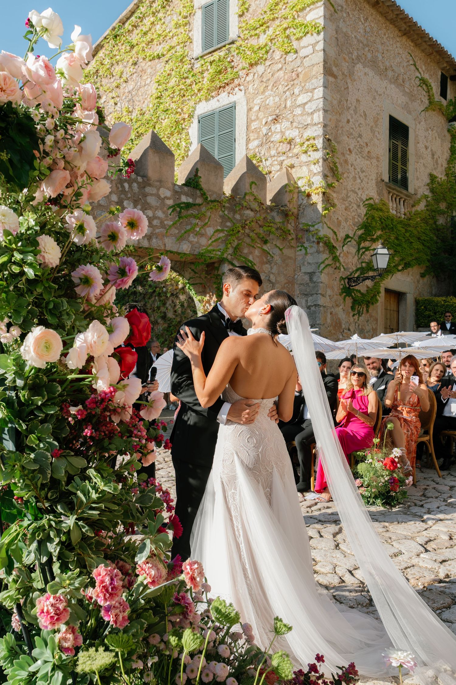 Romantic outdoor wedding ceremony with floral decorations against a rustic stone wall backdrop.
