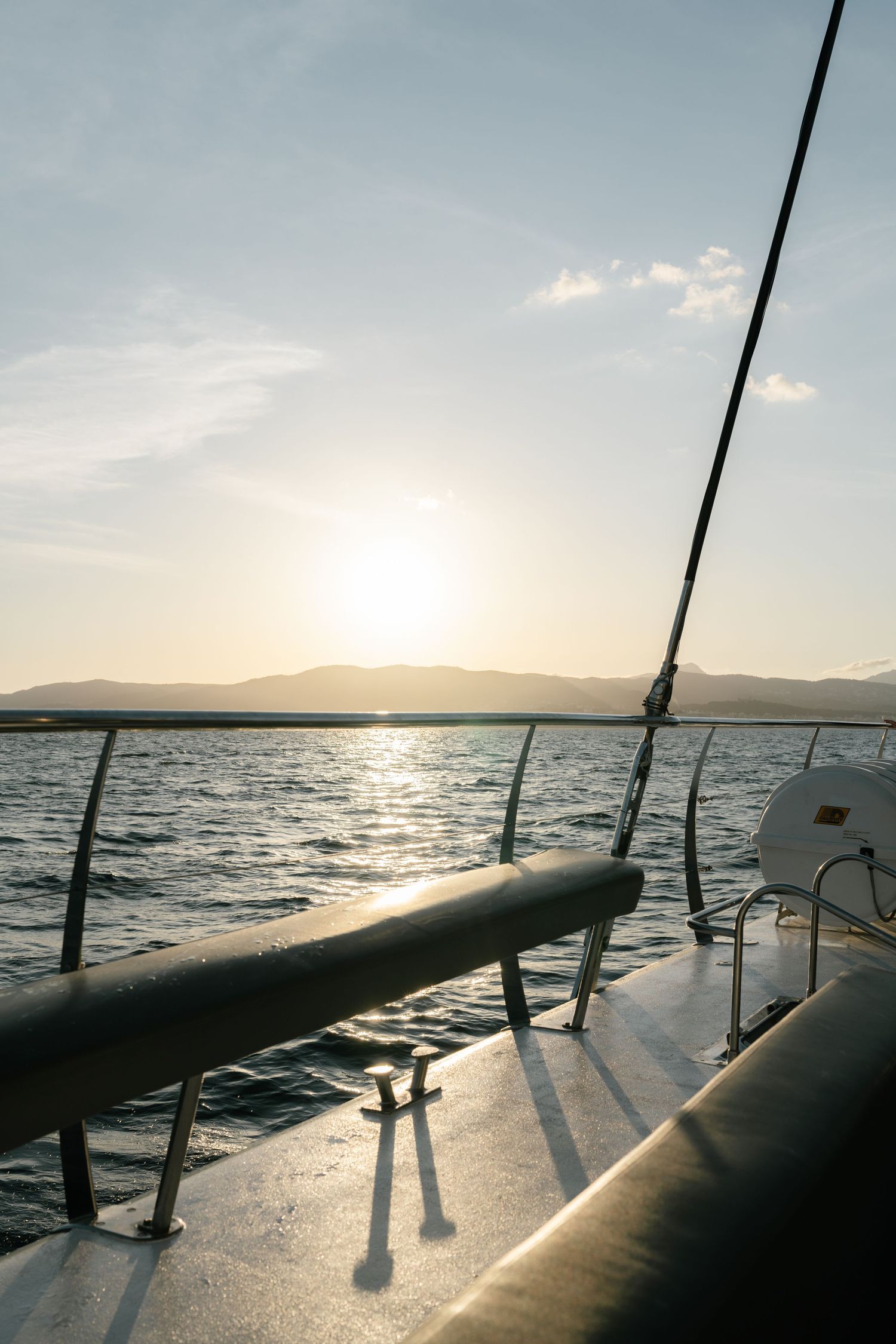 Scenic ocean view from a boat deck at sunset with railing silhouettes against the glowing horizon.
