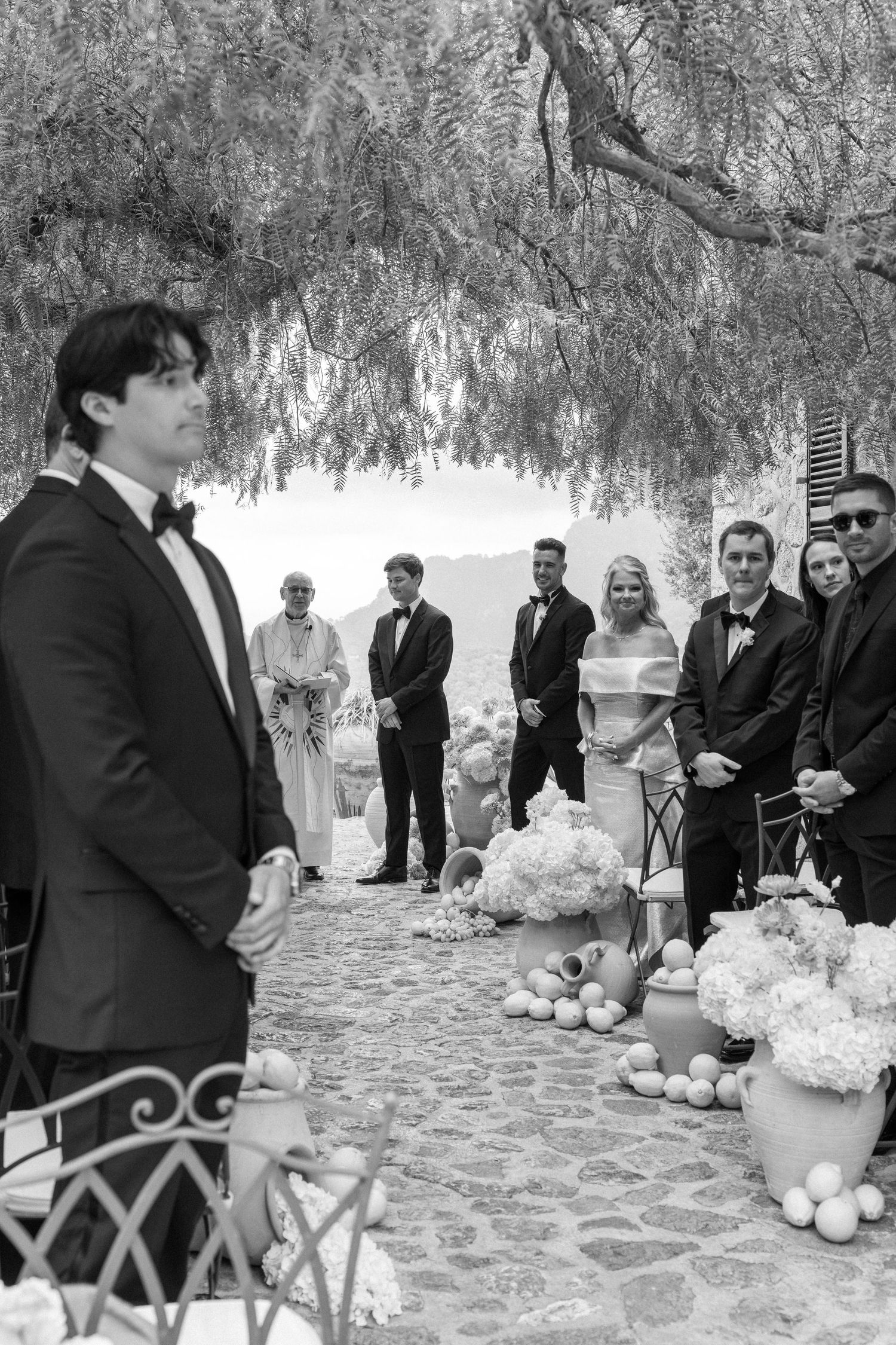 A formal wedding ceremony setup outdoors under drooping willow tree branches with black and white decor.