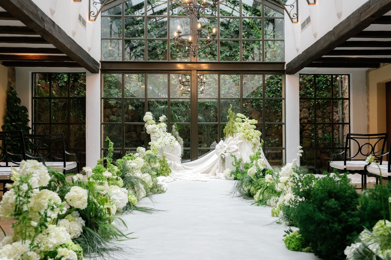 A rustic wedding venue with white floral arrangements and greenery decorating a glass-enclosed walkway.