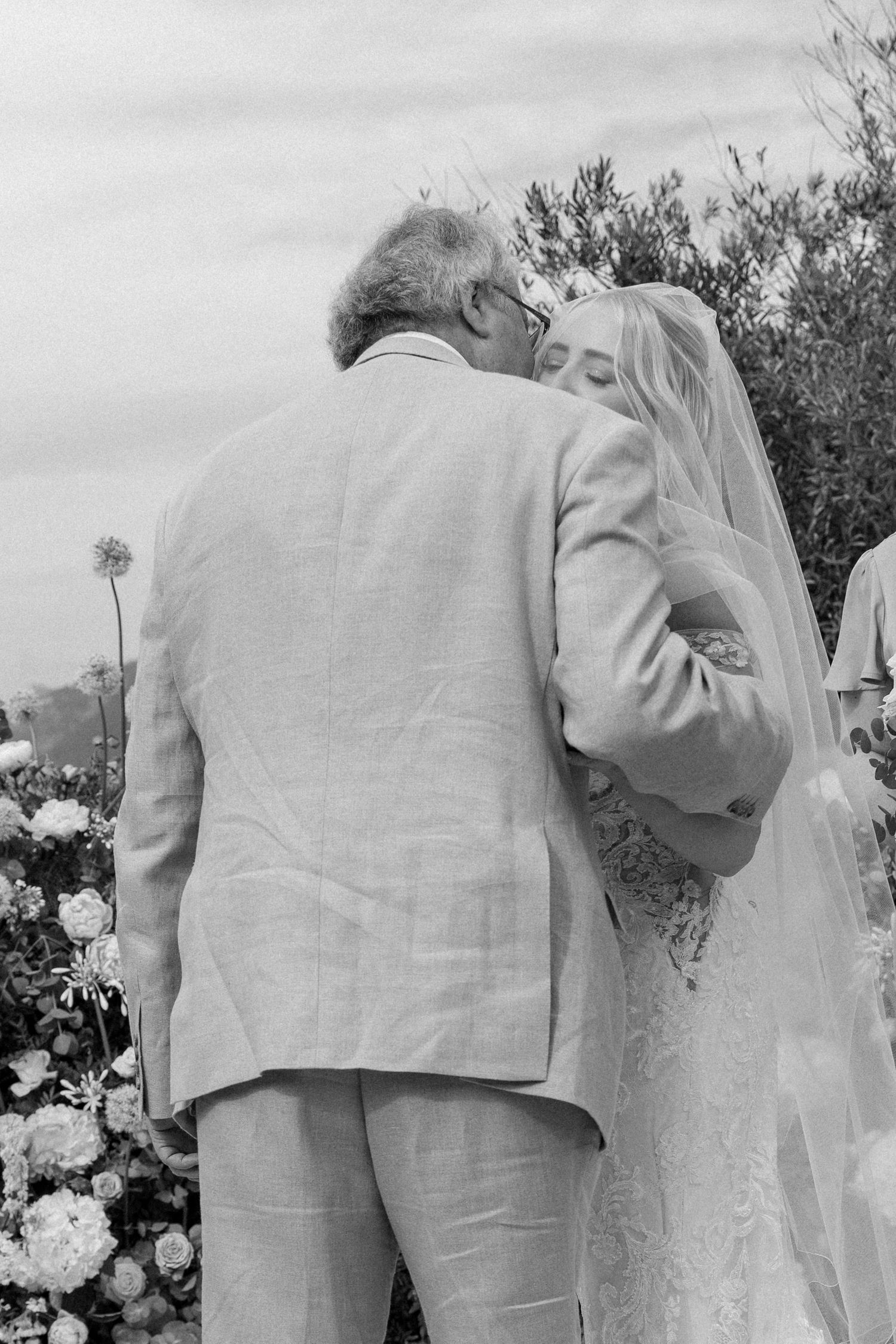 Close-up details of wedding attire in soft gray and white tones against a garden backdrop.