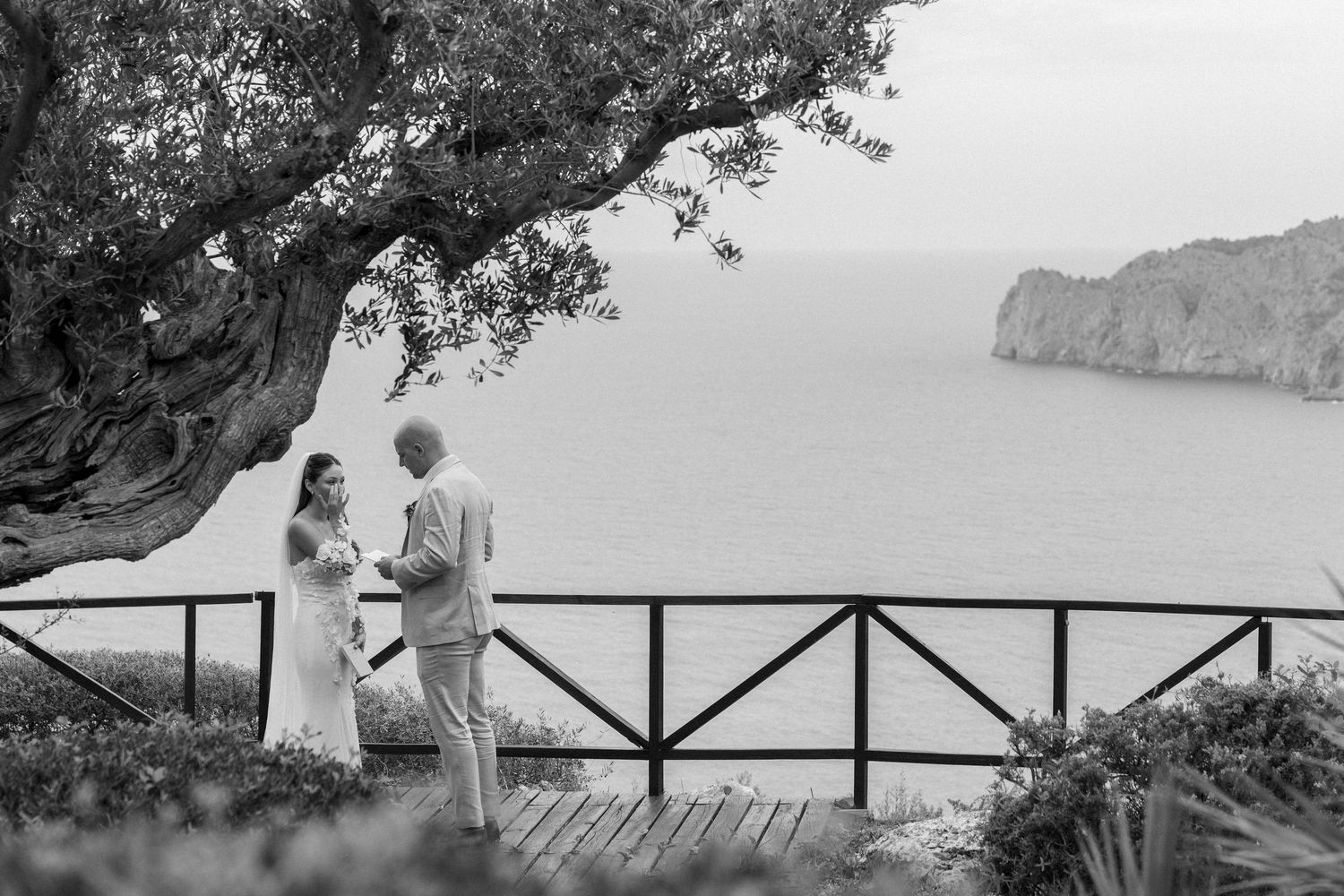 A scenic wedding photo shoot on a coastal overlook with mountains and ocean in the background.