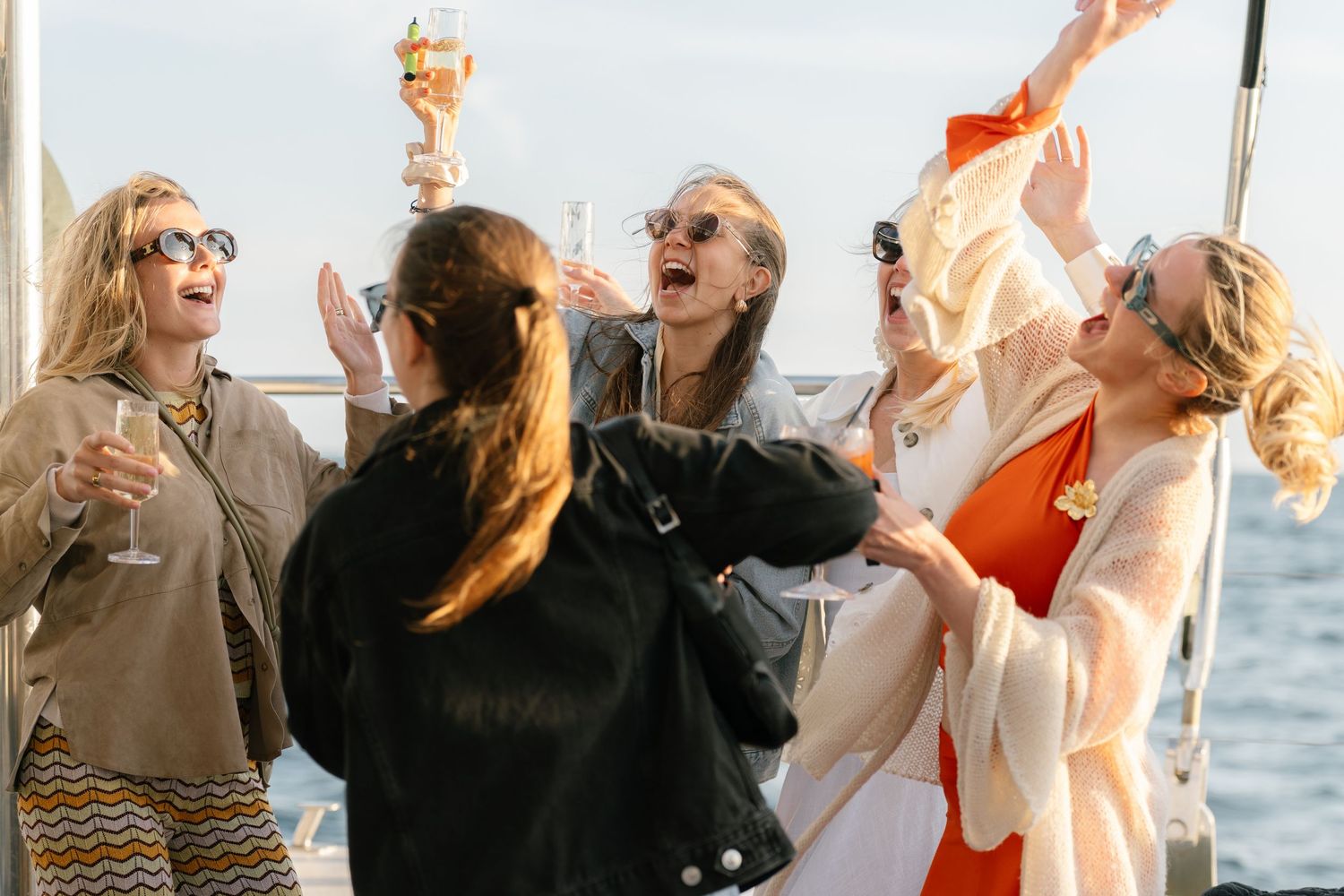 A group celebrates with drinks and laughter during a sunset boat party.