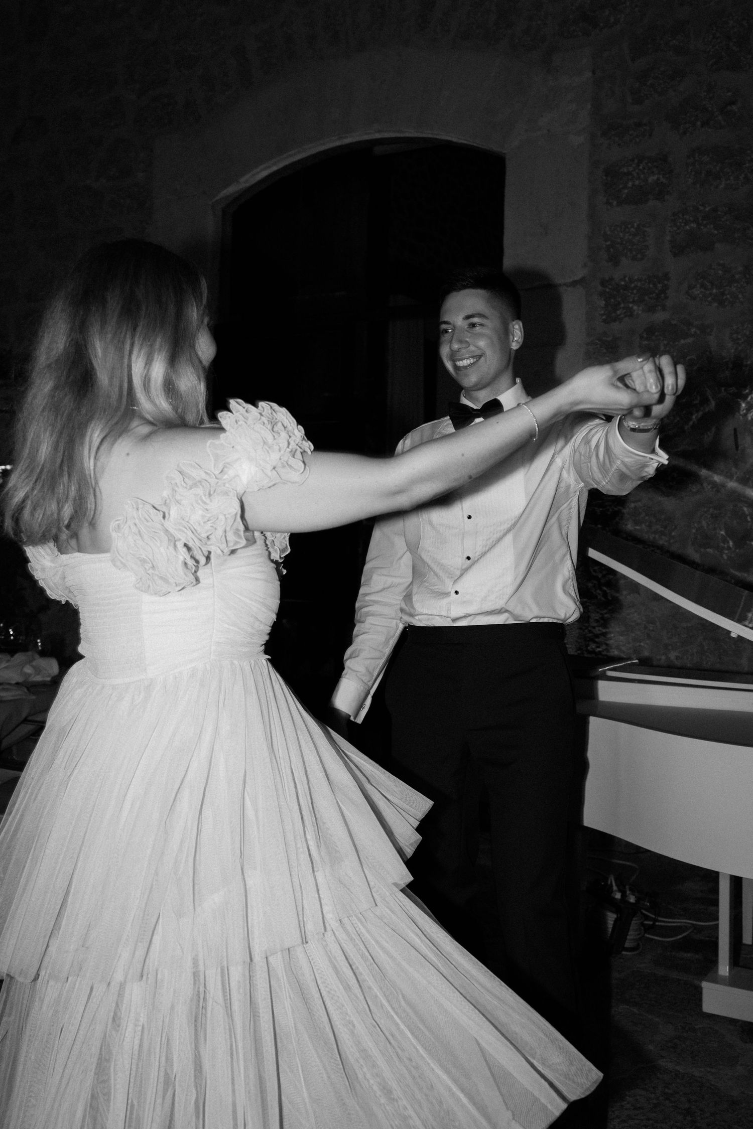 Guests dancing in formal attire at a wedding reception with stone walls in the background.