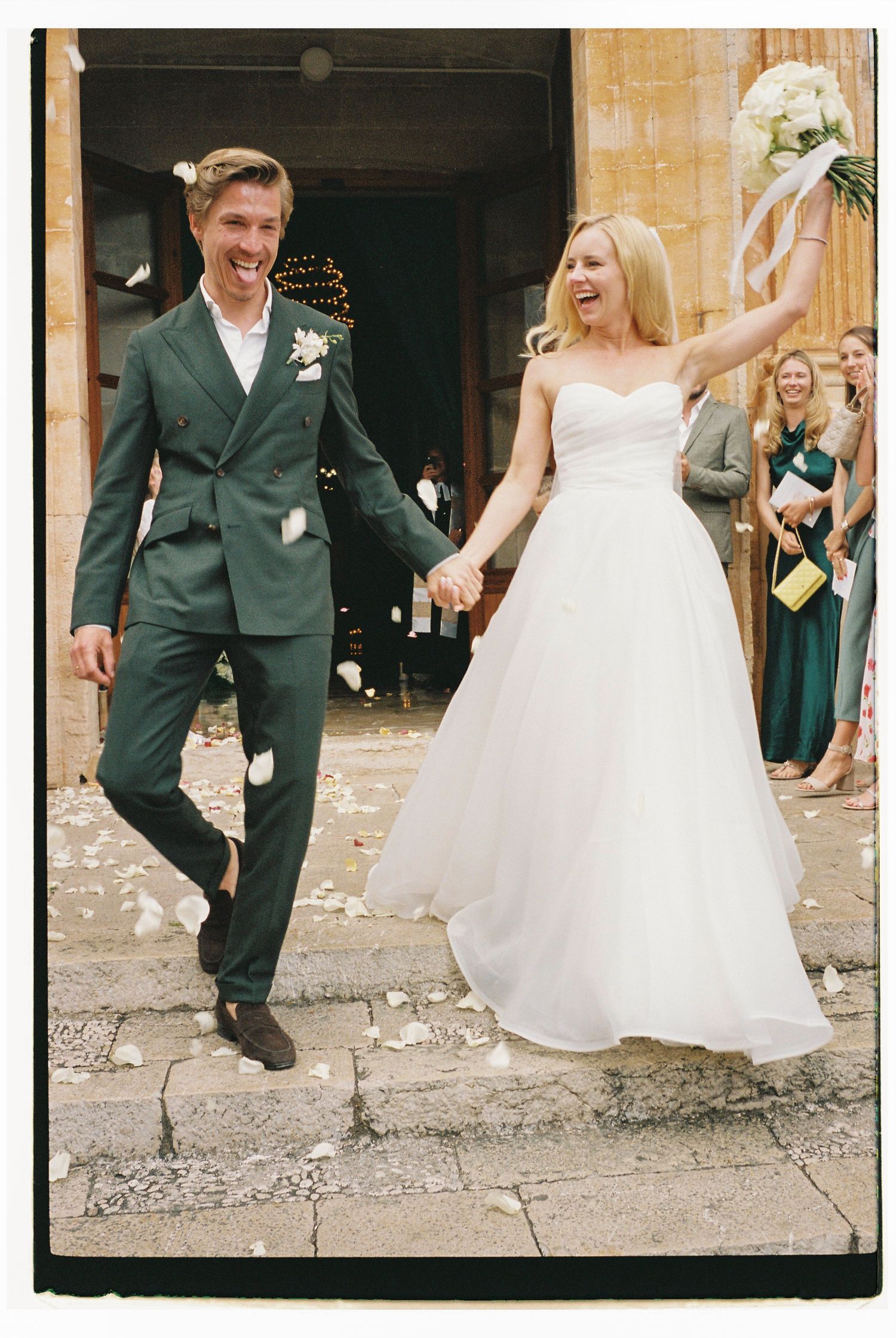 Newlyweds joyfully exit their ceremony while guests celebrate on stone pathway.