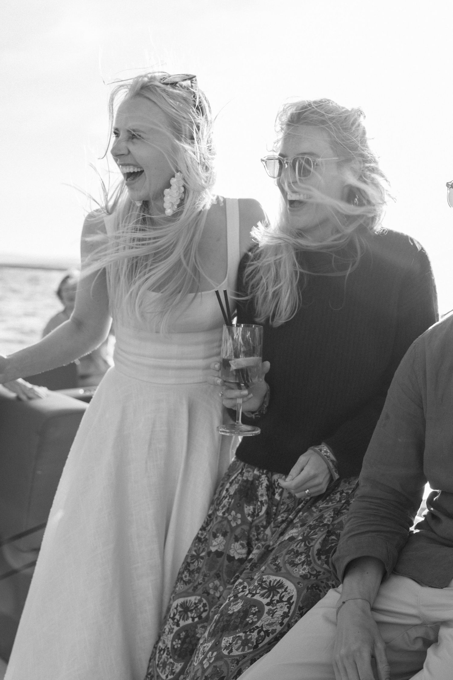 Two women in casual attire share laughter while enjoying drinks on a boat.