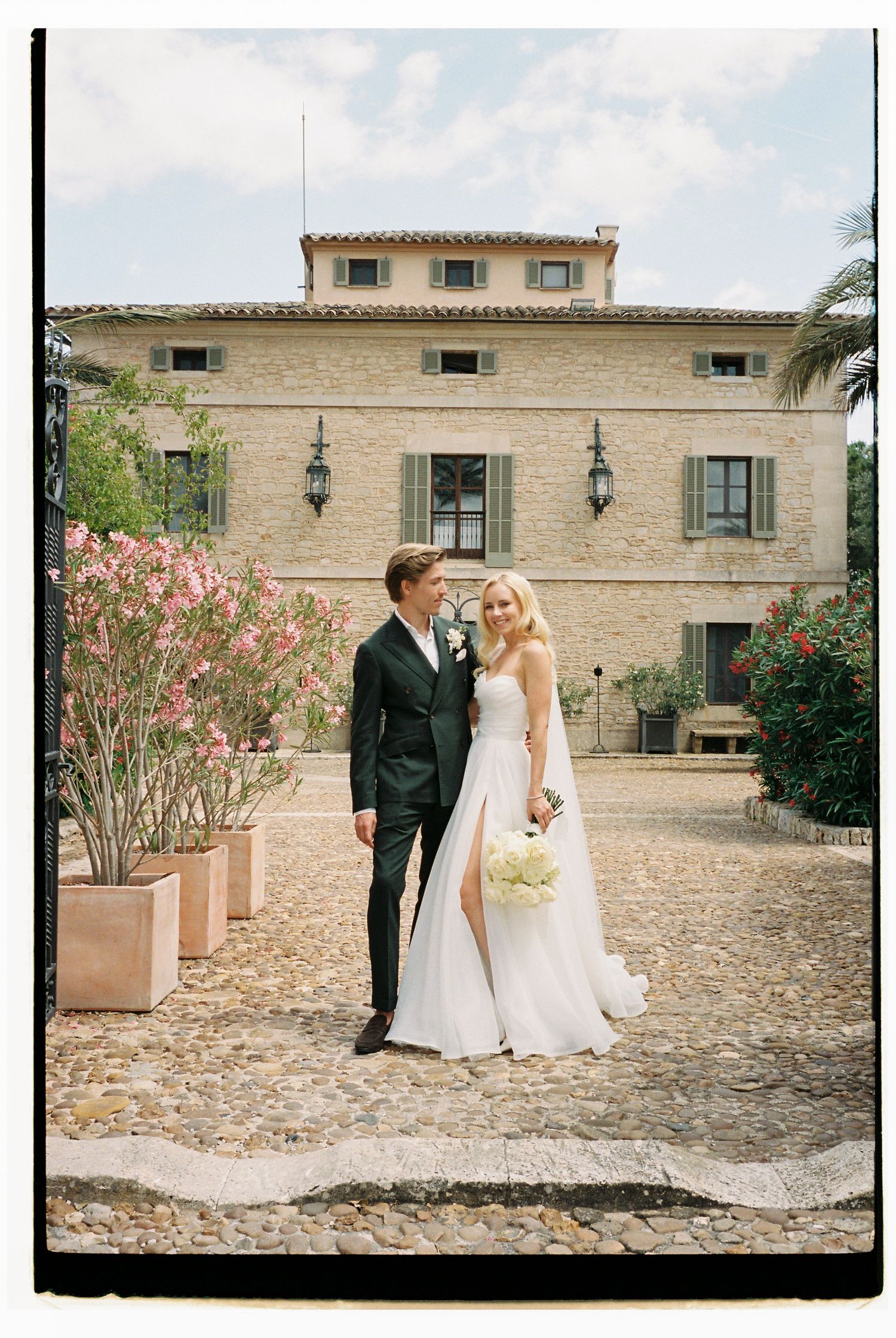 Newlyweds pose together outside a Mediterranean stone villa on their wedding day.