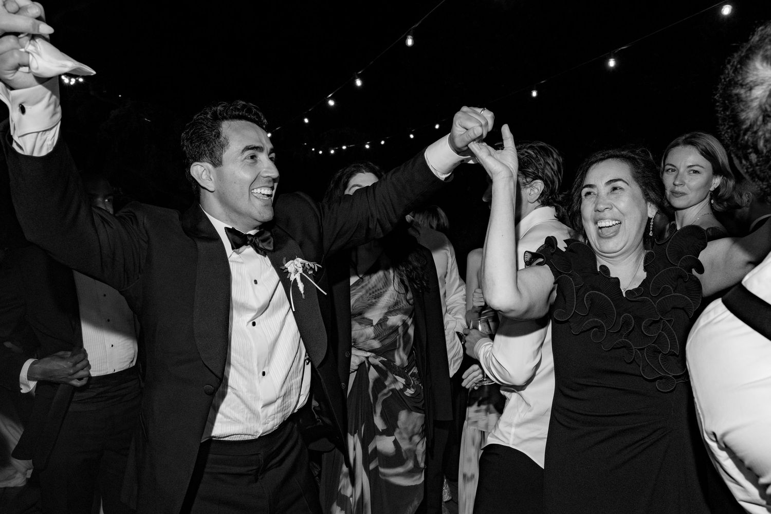 Black and white photo of a man in tuxedo and woman in black dress dancing joyfully at a wedding reception.