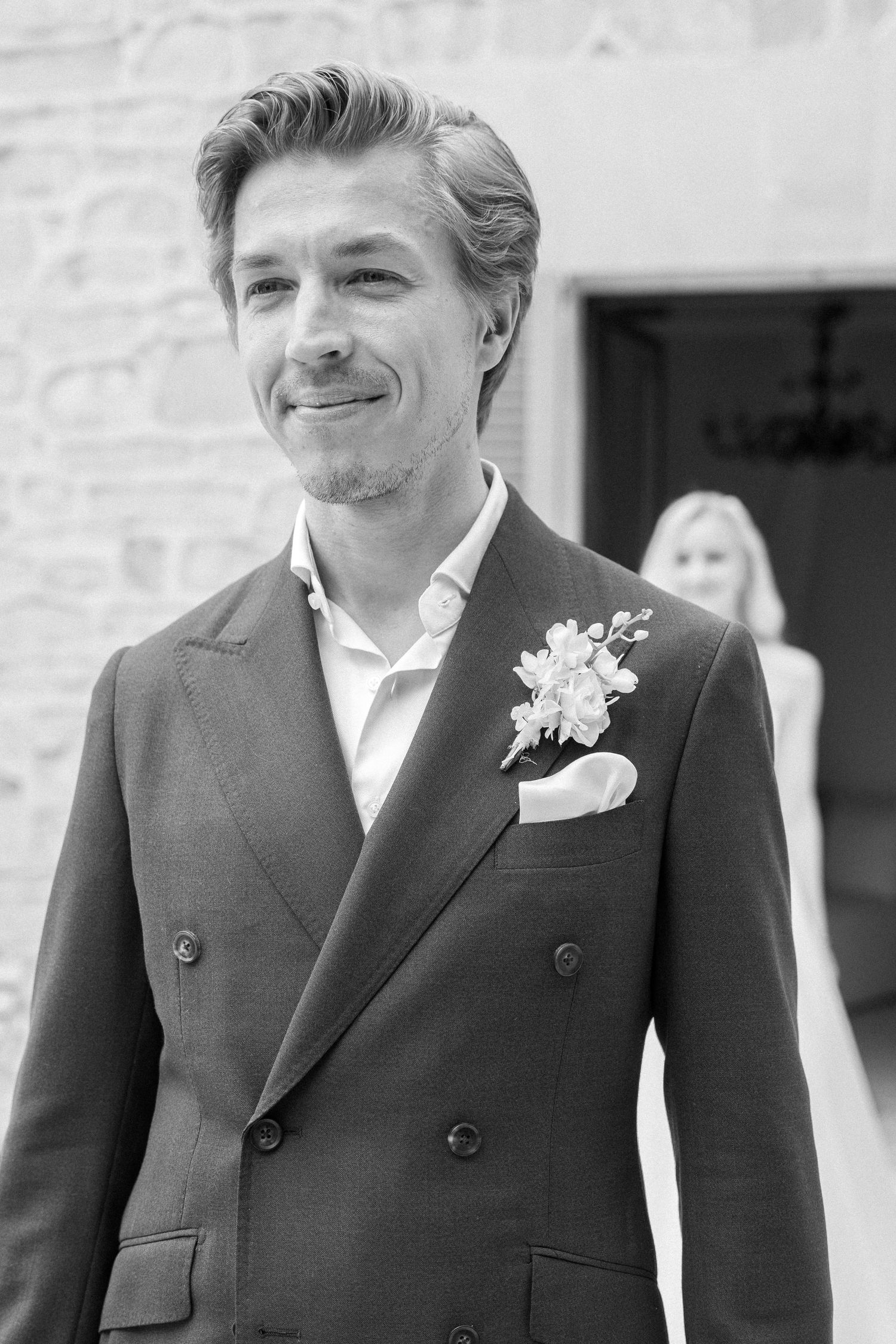 Close-up black and white portrait shots of a groom wearing a dark suit with boutonniere at a wedding.