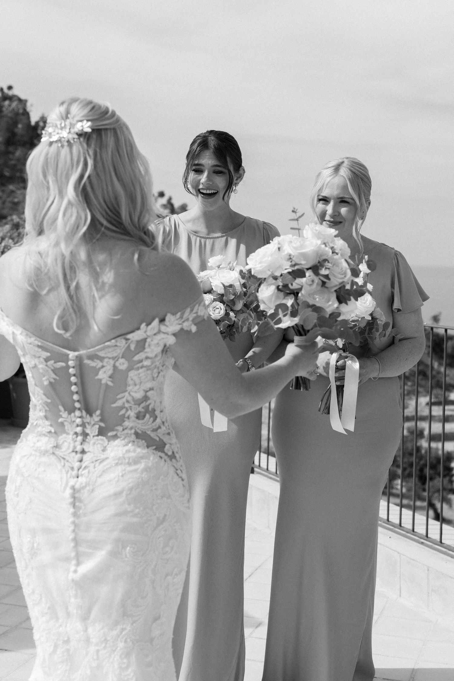 A wedding party wearing light gray dresses poses together with bouquets against a scenic mountain backdrop.