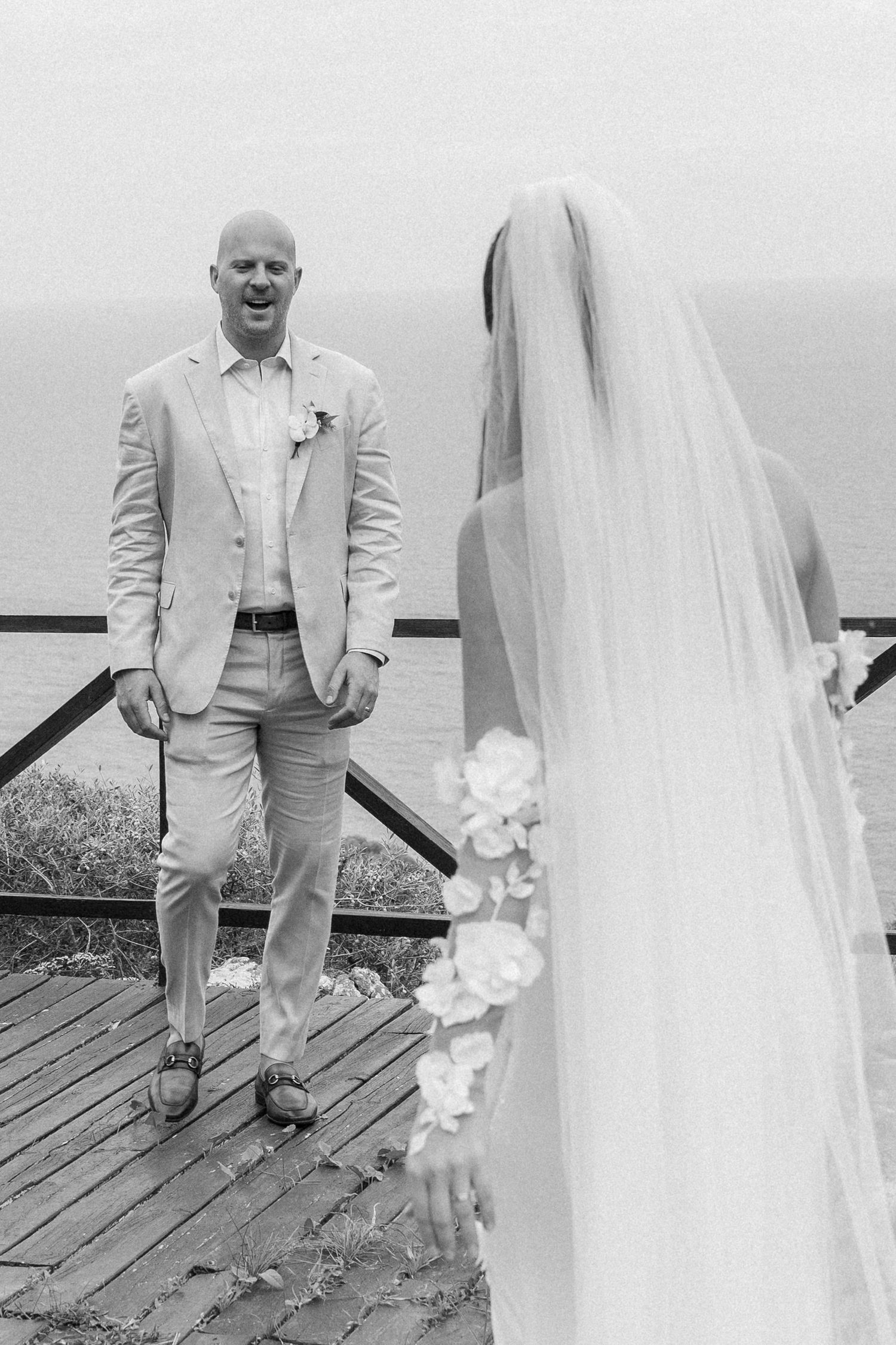 Black and white wedding photos showing intimate moments on a wooden deck overlooking the sea.