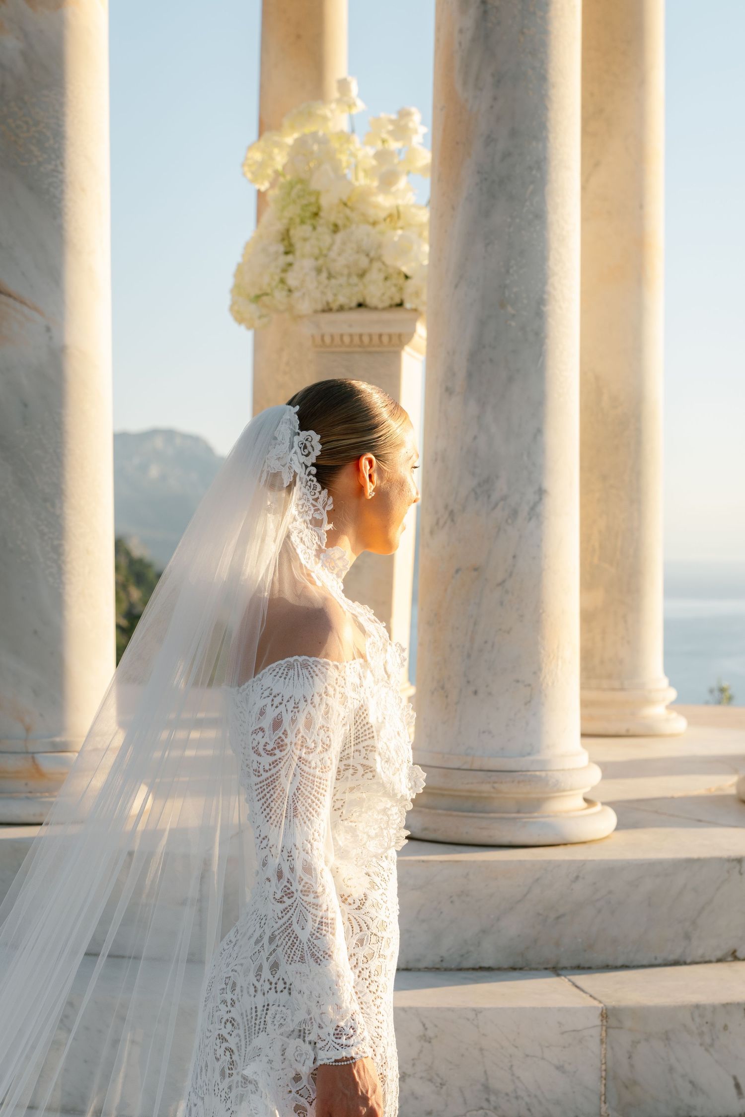 Sun-drenched wedding photography session among classical white columns with flowing veil.