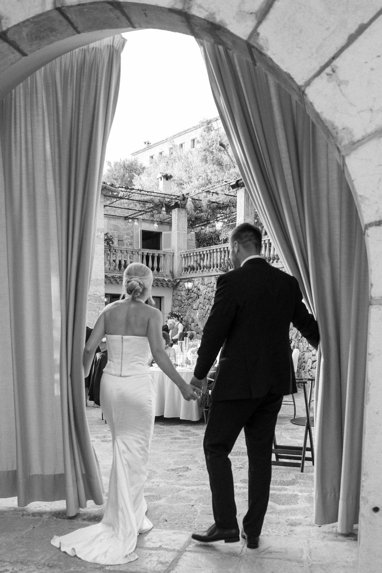 Wedding couple walking through elegant archways with flowing curtains.