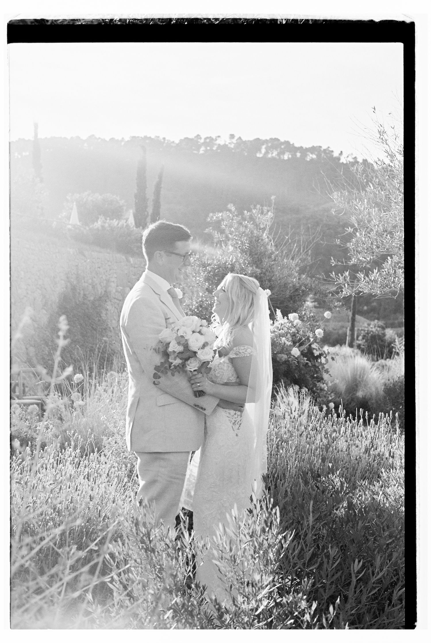 Dreamy sunlit wedding portrait in a wildflower field with mountains in background.
