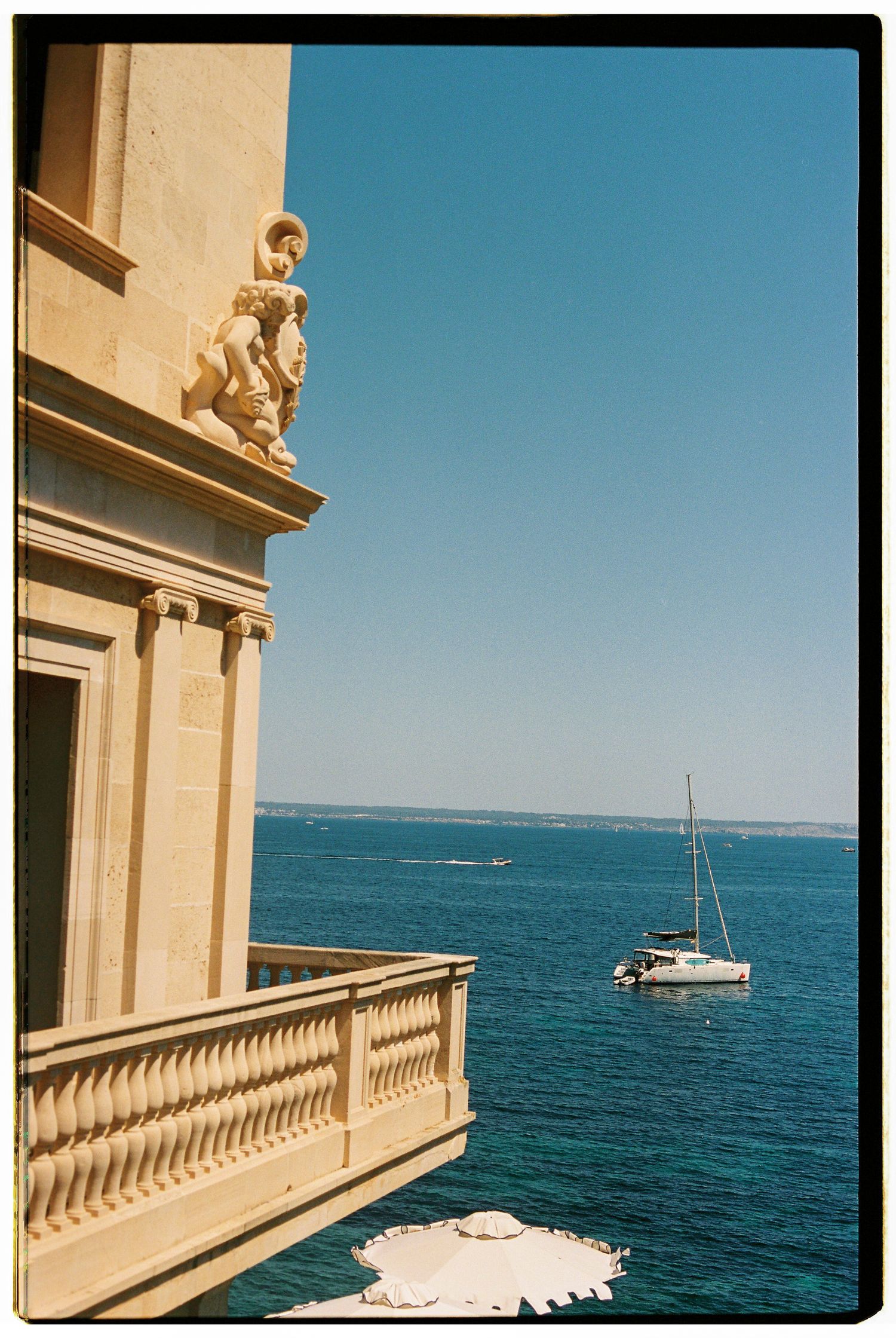 Luxury seaside balcony views of Mediterranean waters with sailboats and yachts dotting the blue horizon.