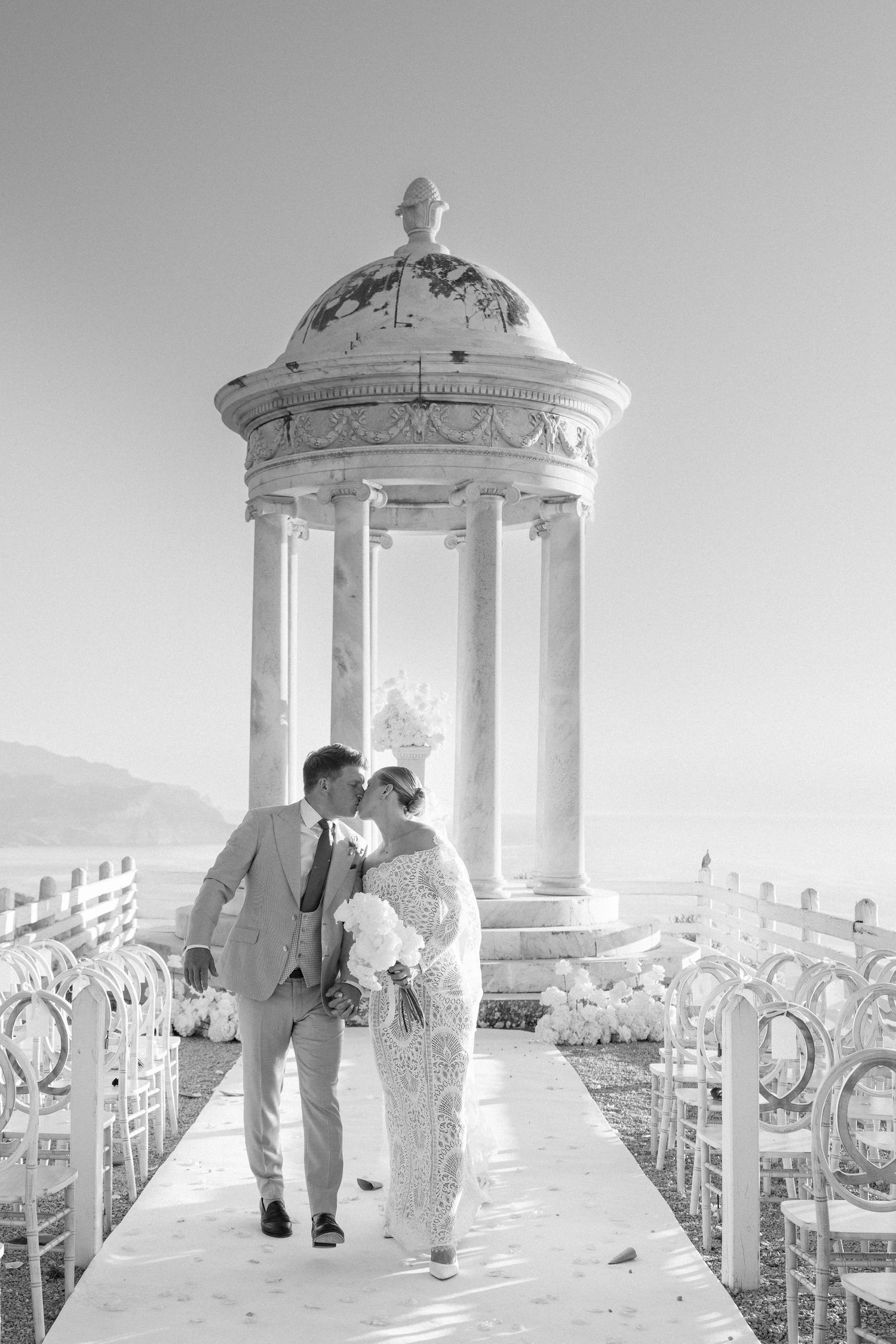 Wedding couple shares romantic moments in elegant white gazebo overlooking scenic mountain views.