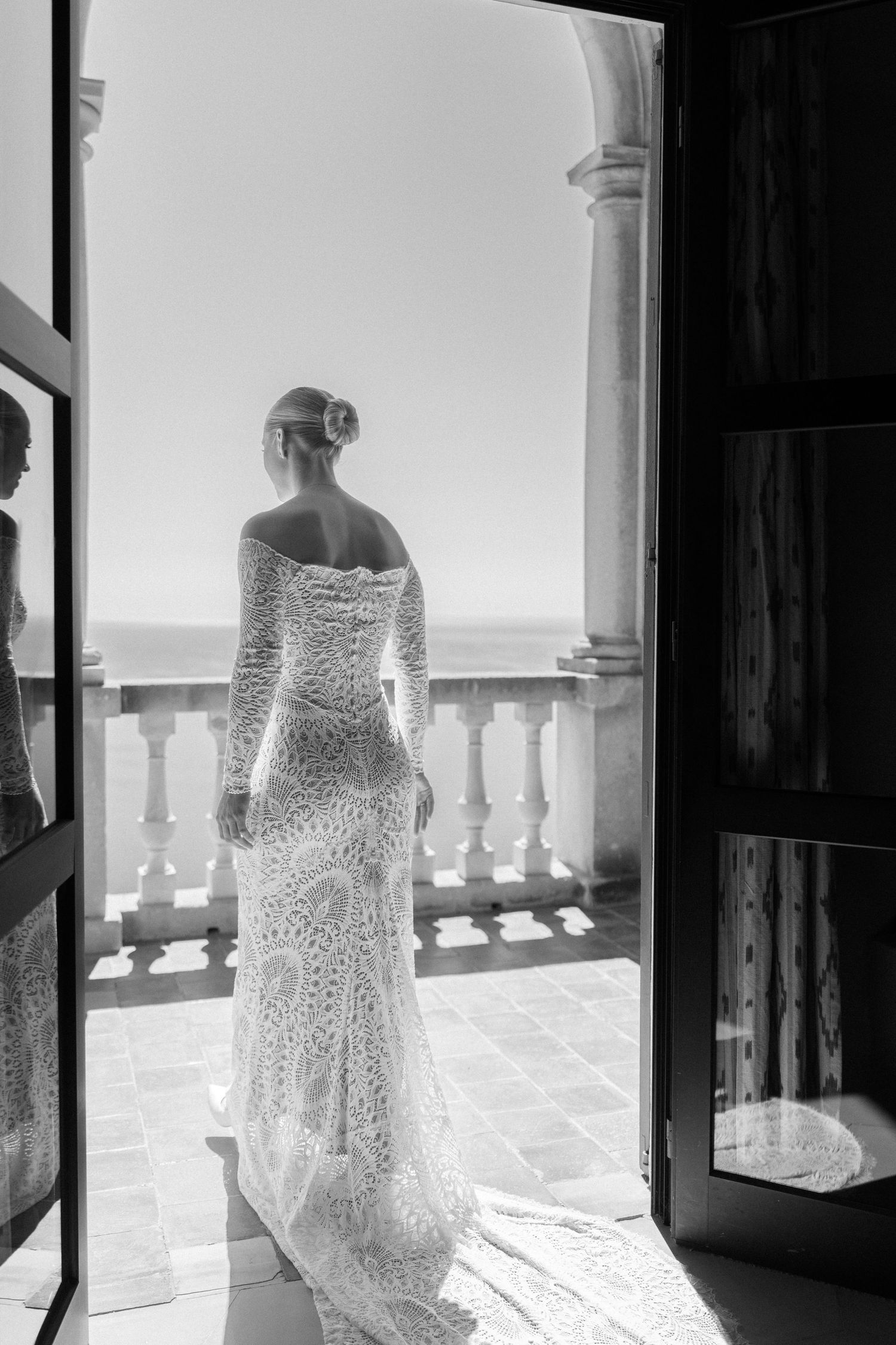 Silhouette of wedding dress against bright balcony windows overlooking the ocean.