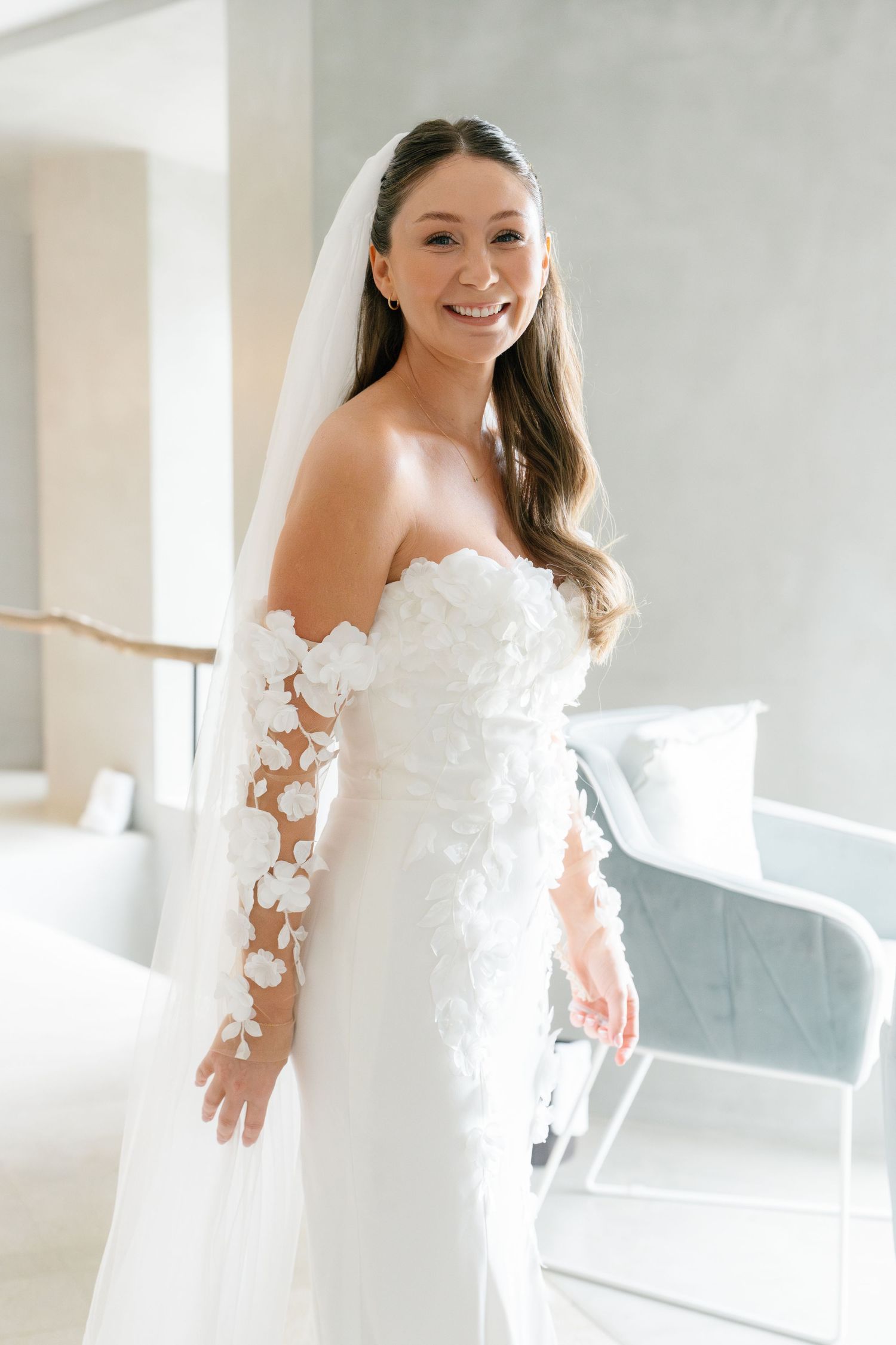 Bride in white gown with floral details poses in bright modern space.