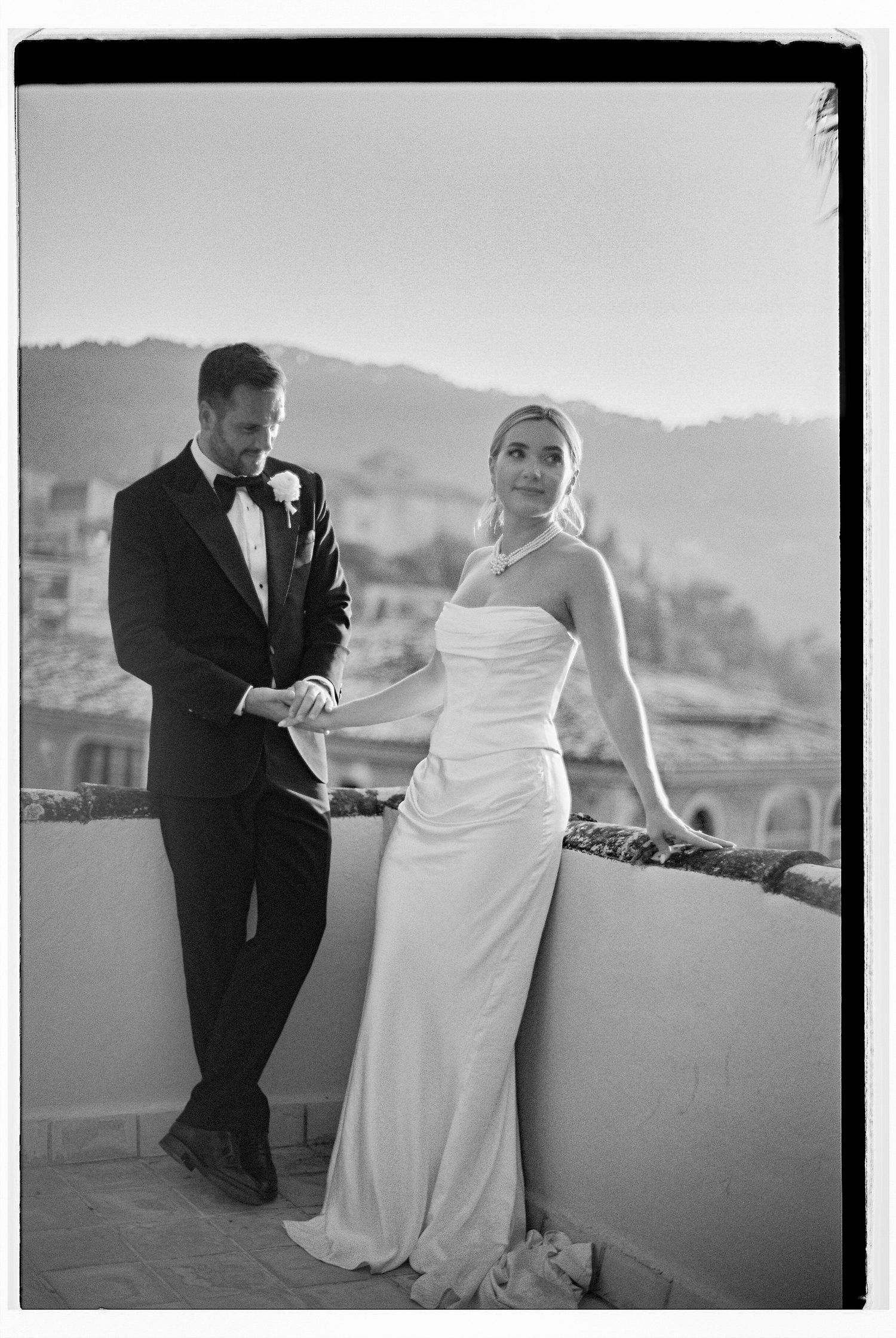 A bride and groom share a playful moment on an outdoor terrace with mountain views.