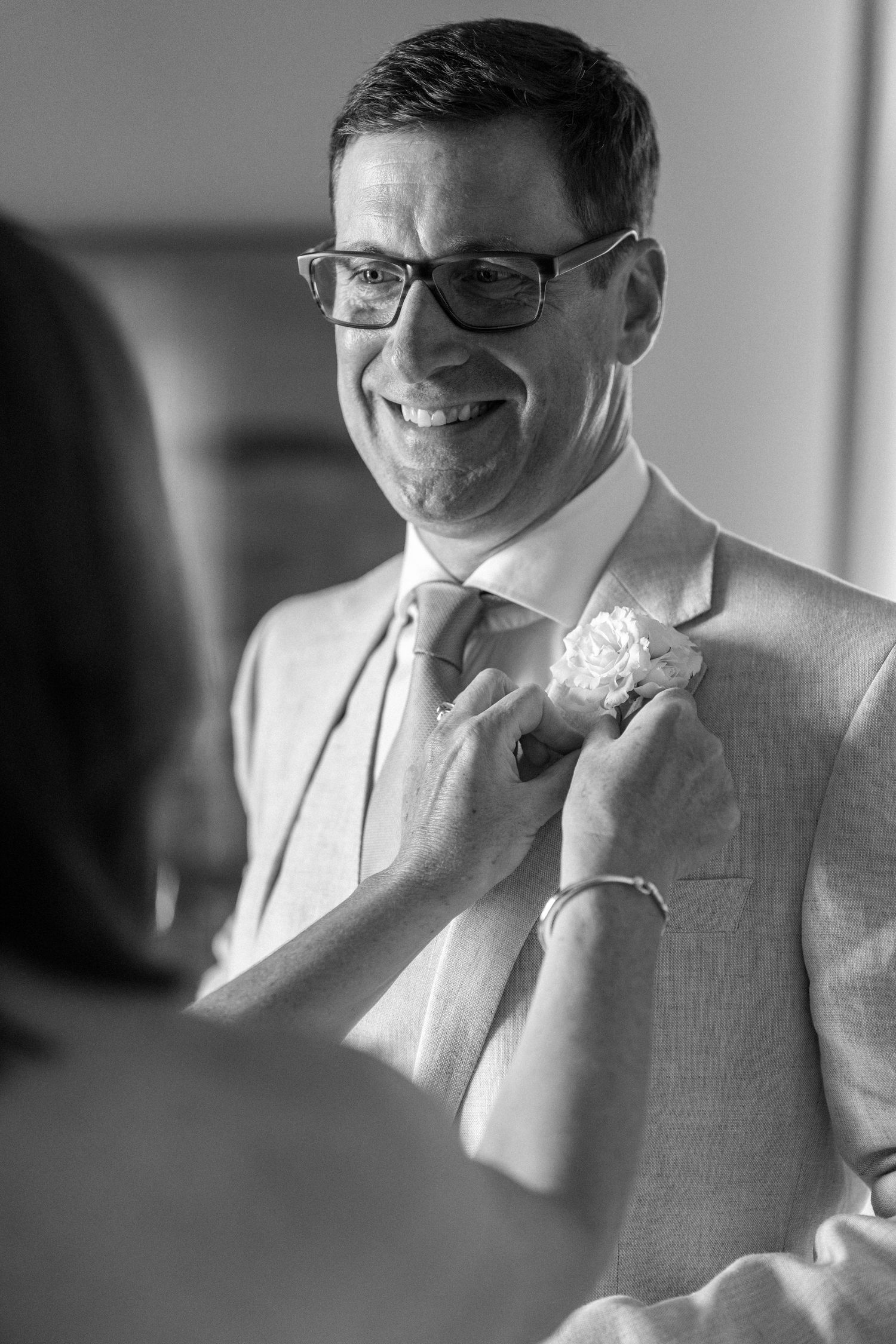 Wedding day portrait of groom in light suit and glasses.
