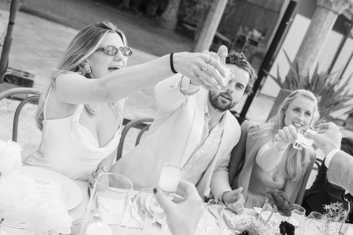 Wedding guests raise glasses in a celebratory toast during an outdoor reception dinner.