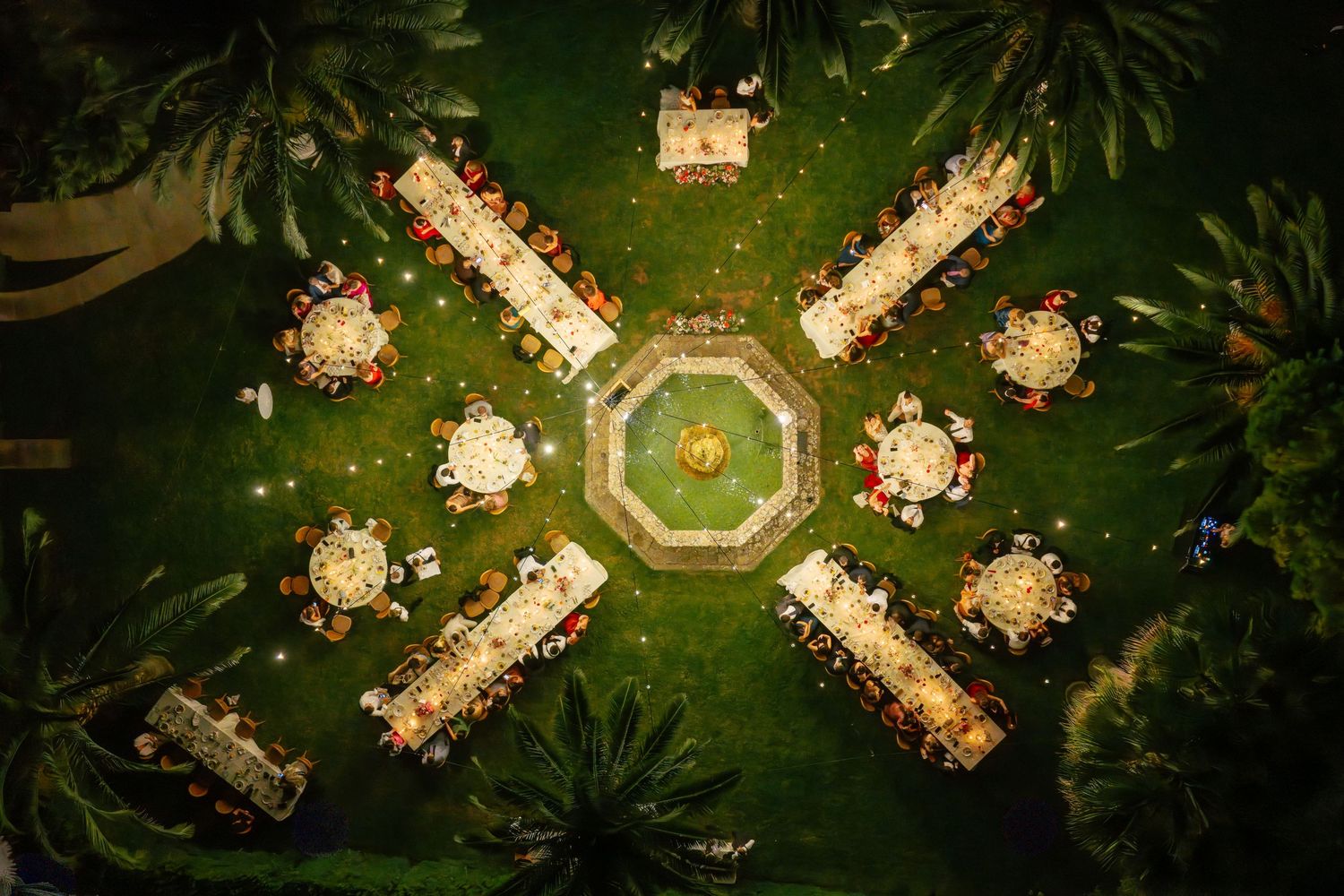 Aerial view of outdoor wedding reception with multiple tables arranged under palm trees.