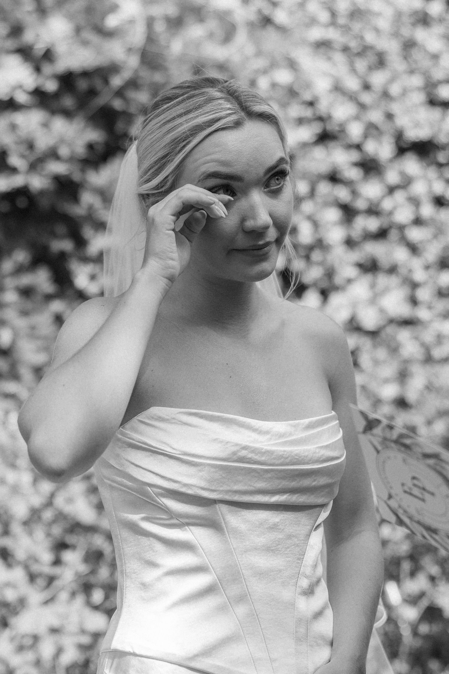 Black and white portrait of bride in strapless wedding dress touching face.
