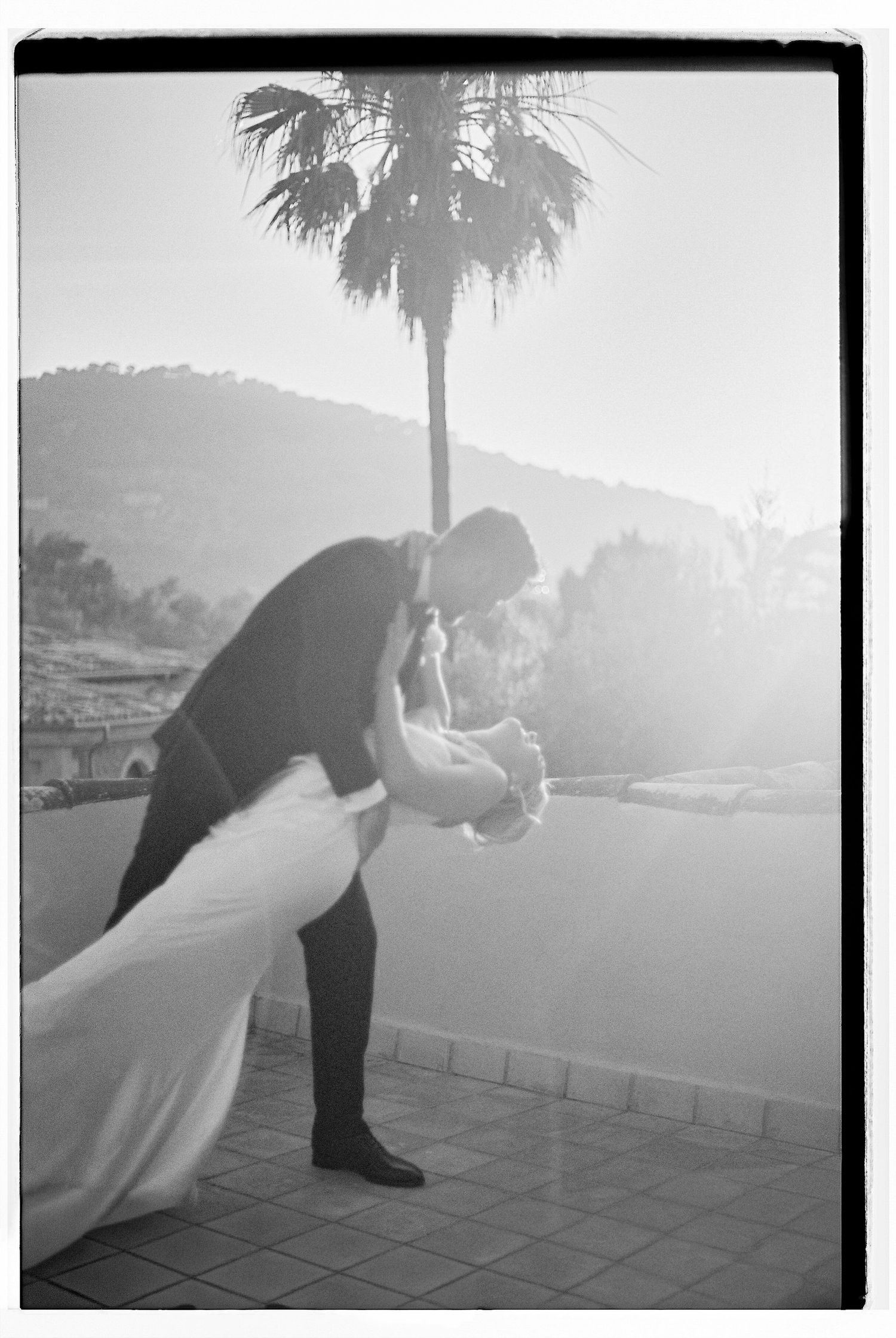 A couple in wedding attire poses dramatically at sunset on a terrace.