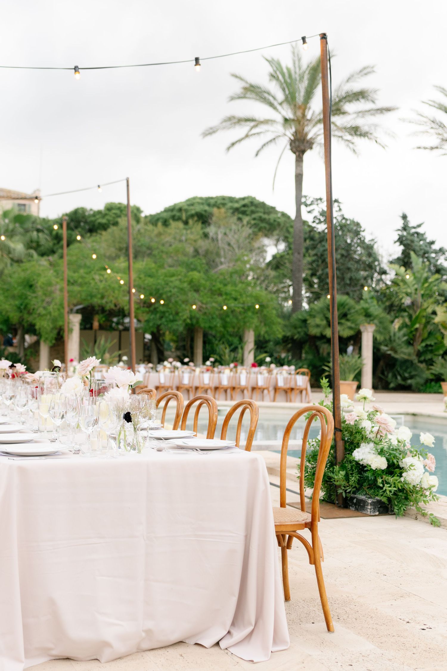 Outdoor wedding reception tables with white linens and wooden chairs under string lights.